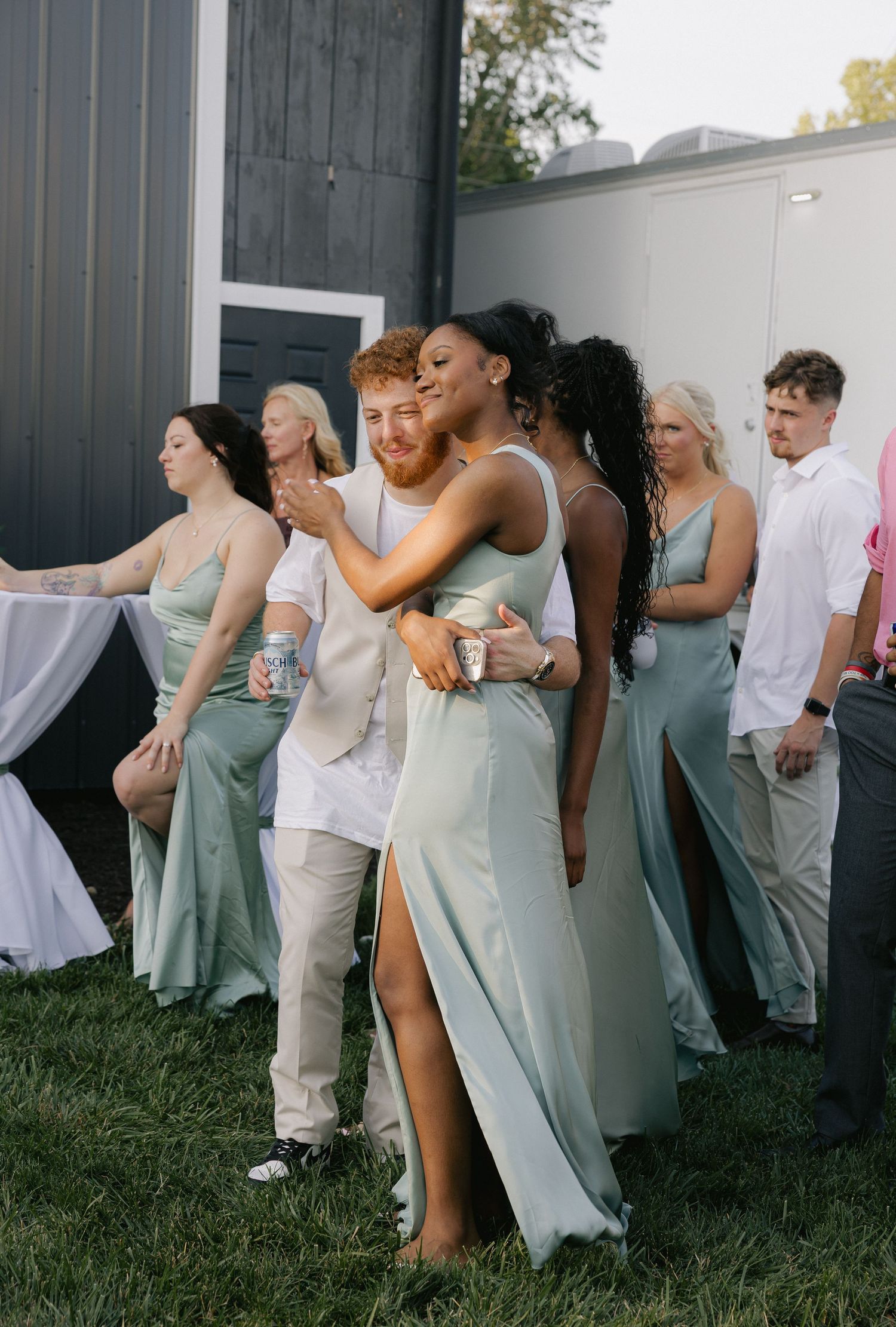 Bridesmaid in sage green dress hugs guest at outdoor wedding reception celebration.