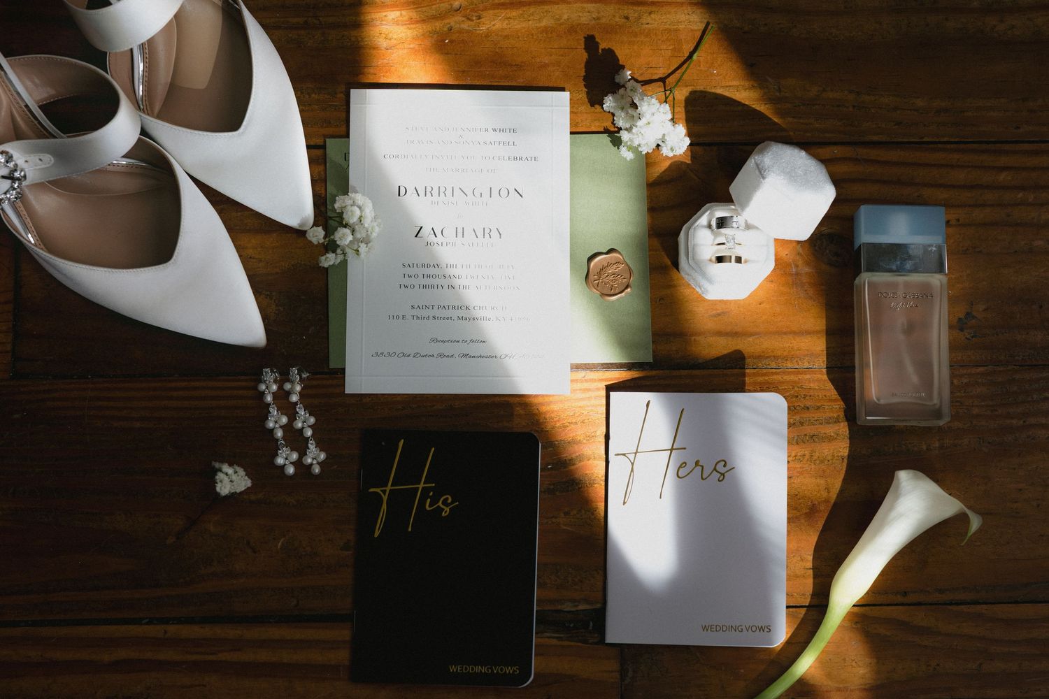 Flat lay of wedding details including invitation, white heels, rings, vows books, and accessories.