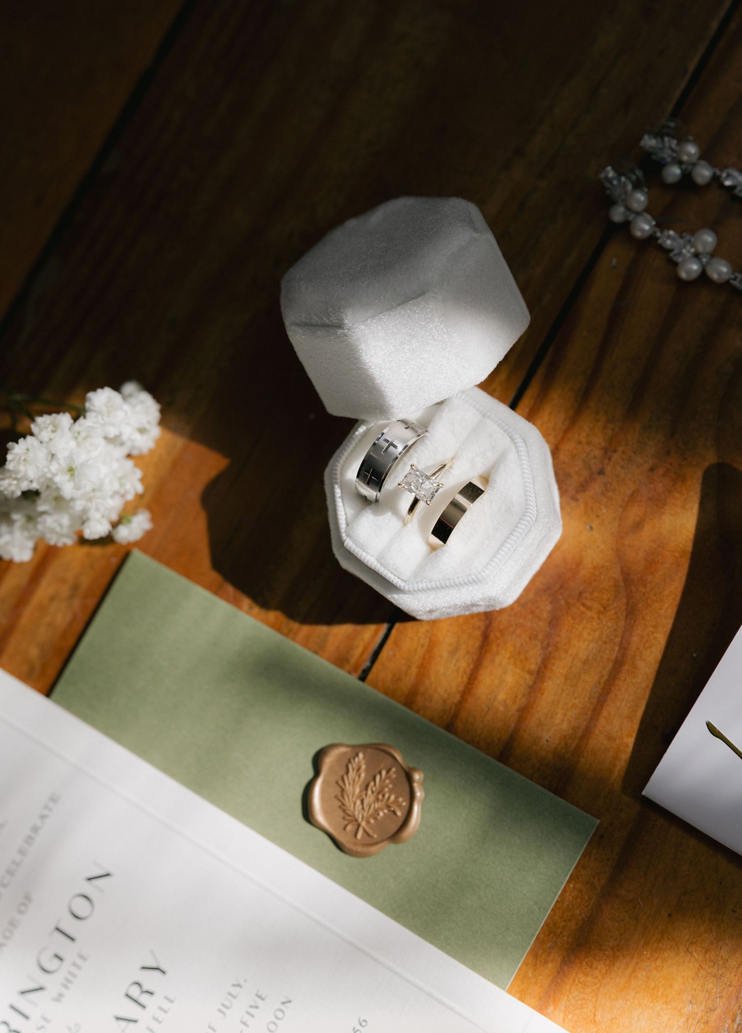Wedding rings displayed in a white velvet octagonal ring box with wax-sealed invitation on wood.