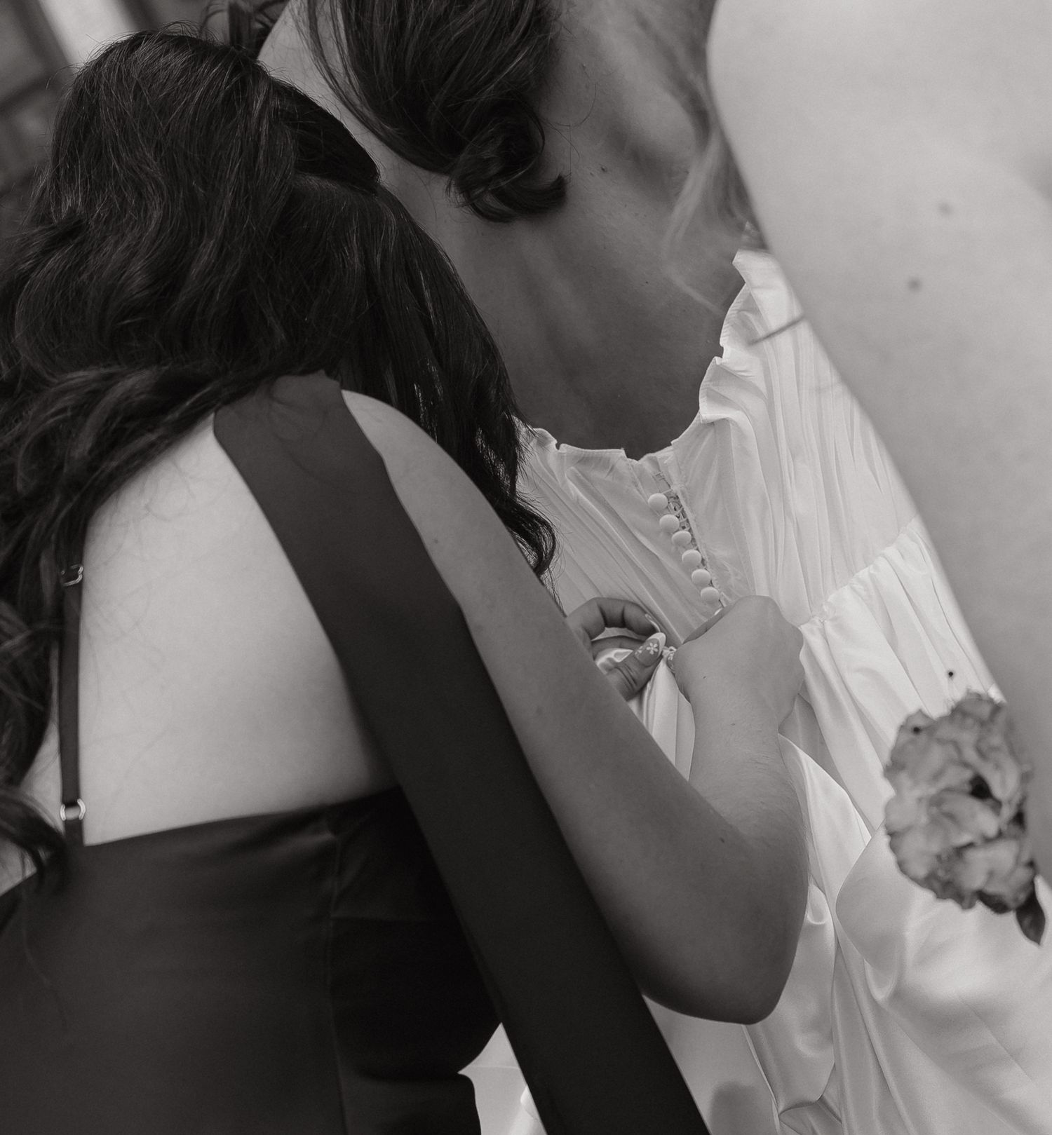 Black and white photo of a bride and bridesmaid embracing at a wedding ceremony.