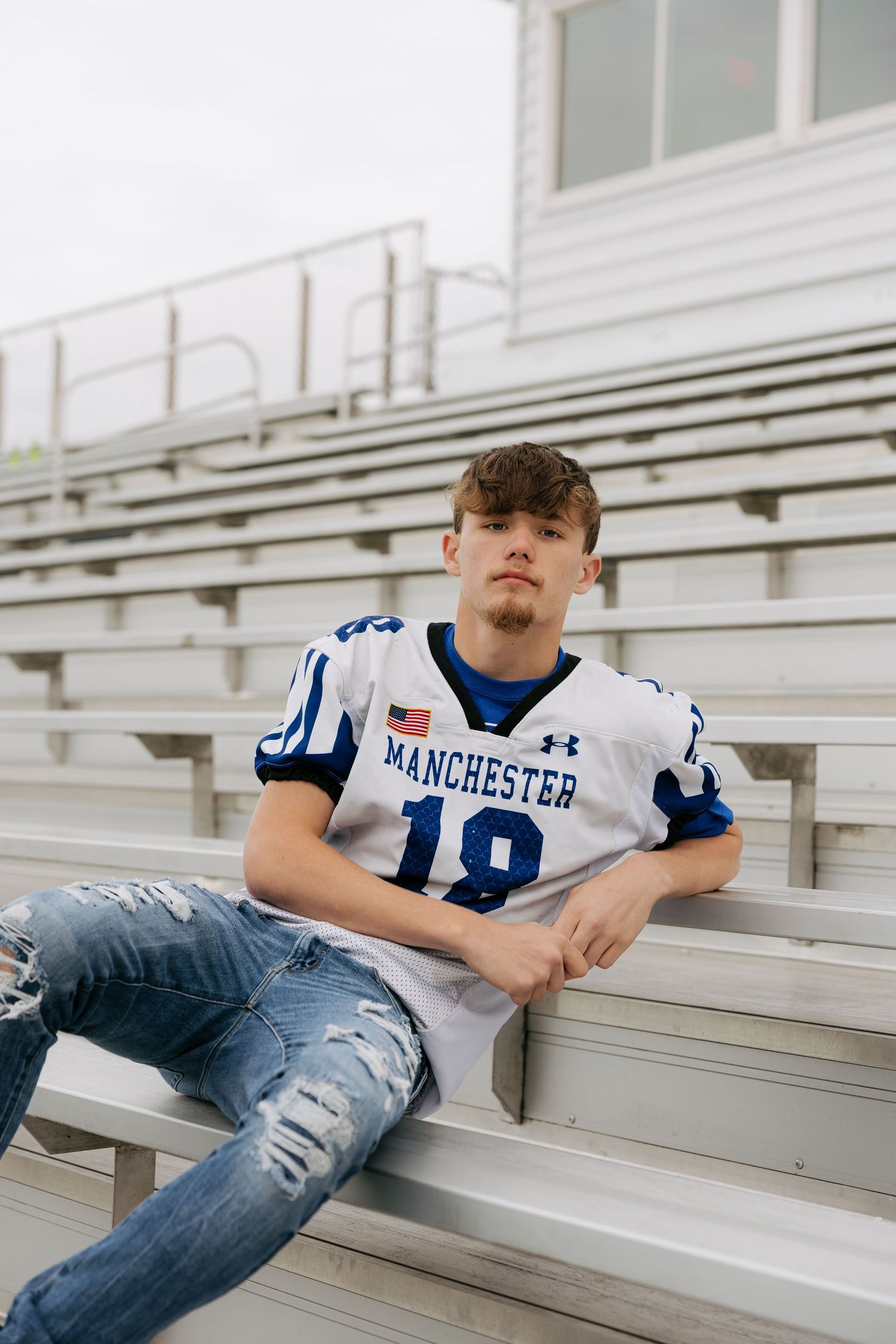 High school senior in Manchester number 18 football jersey sitting in bleachers for senior photos.
