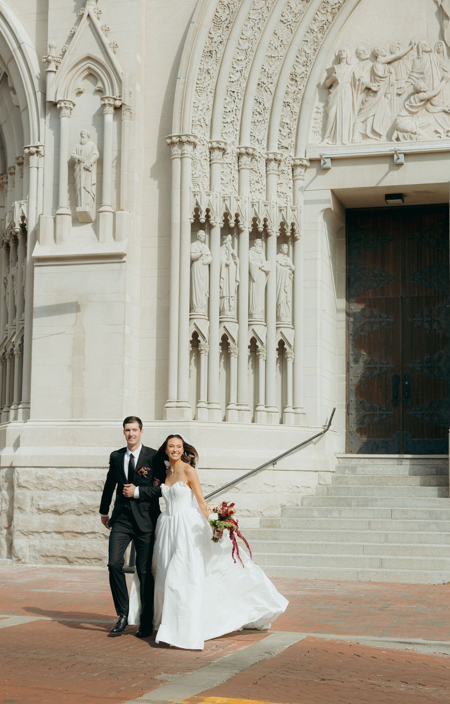 Bride and groom posing outside an ornate church entrance, bride holding a colorful bouquet.