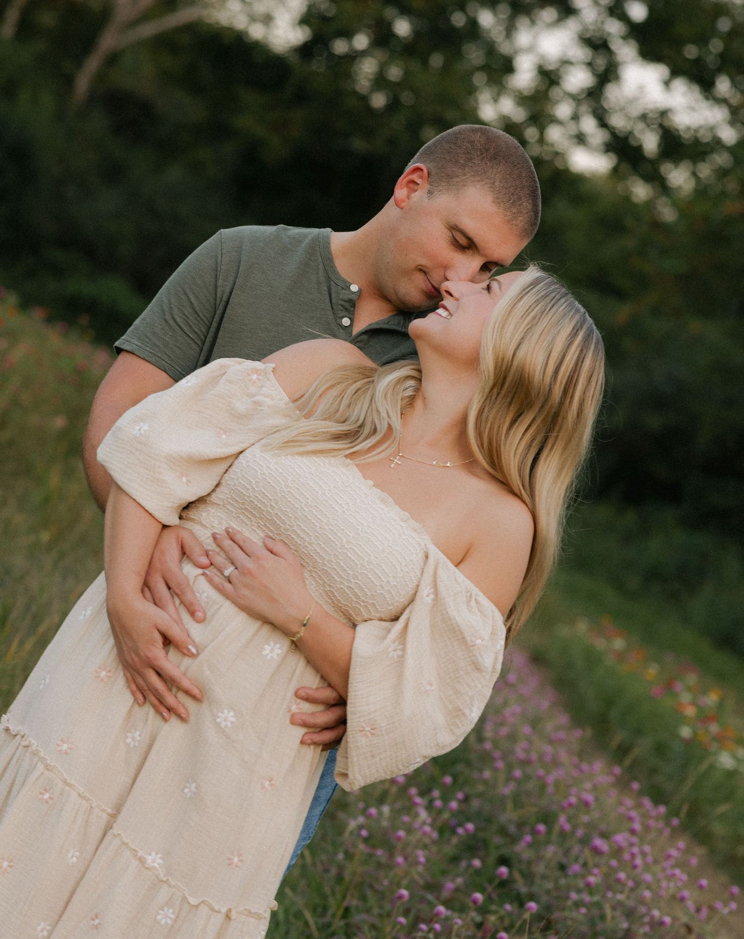 Couple sharing a romantic kiss in a blooming wildflower field at golden hour.