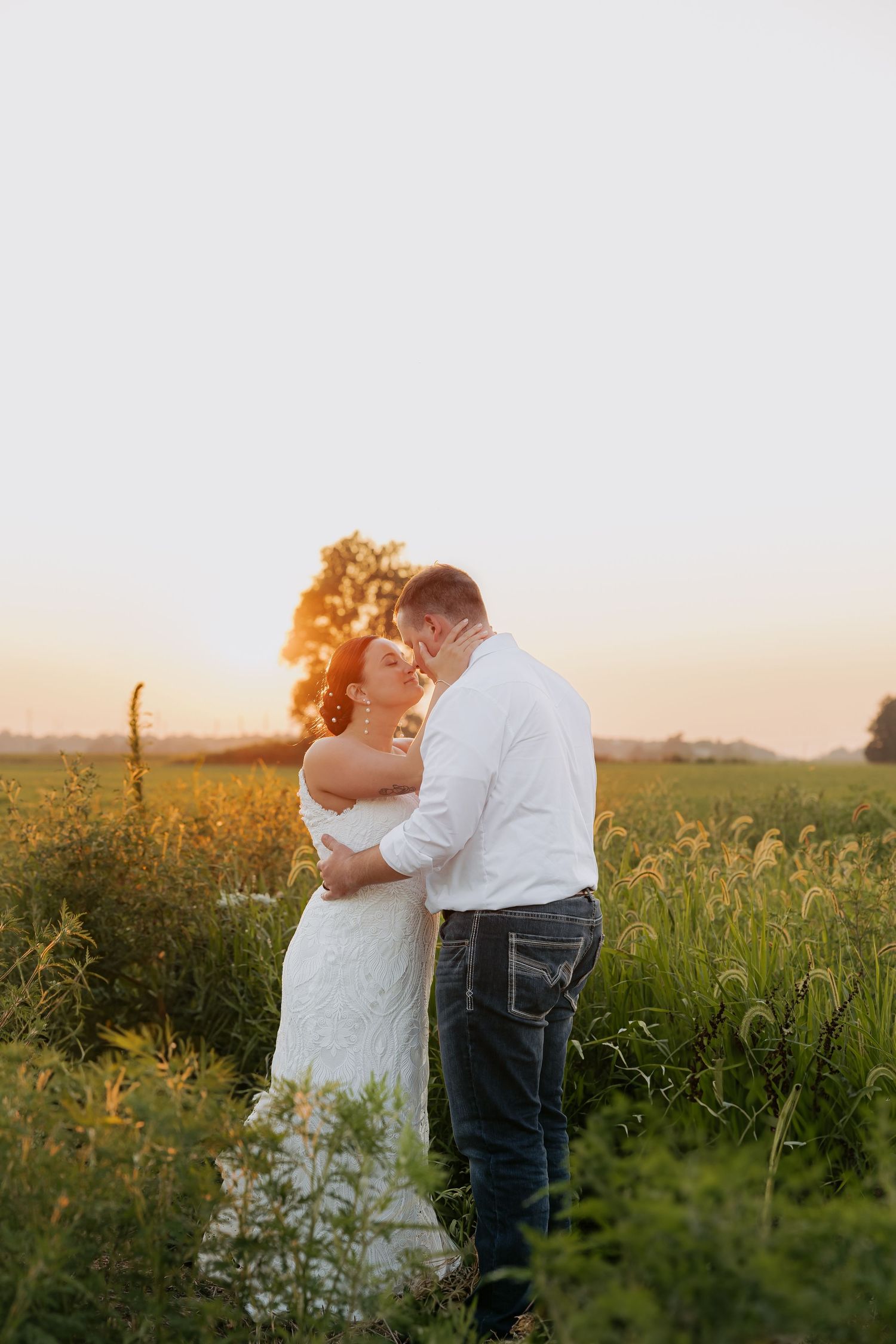 Bride and groom sharing a romantic kiss in a golden sunlit field at sunset.