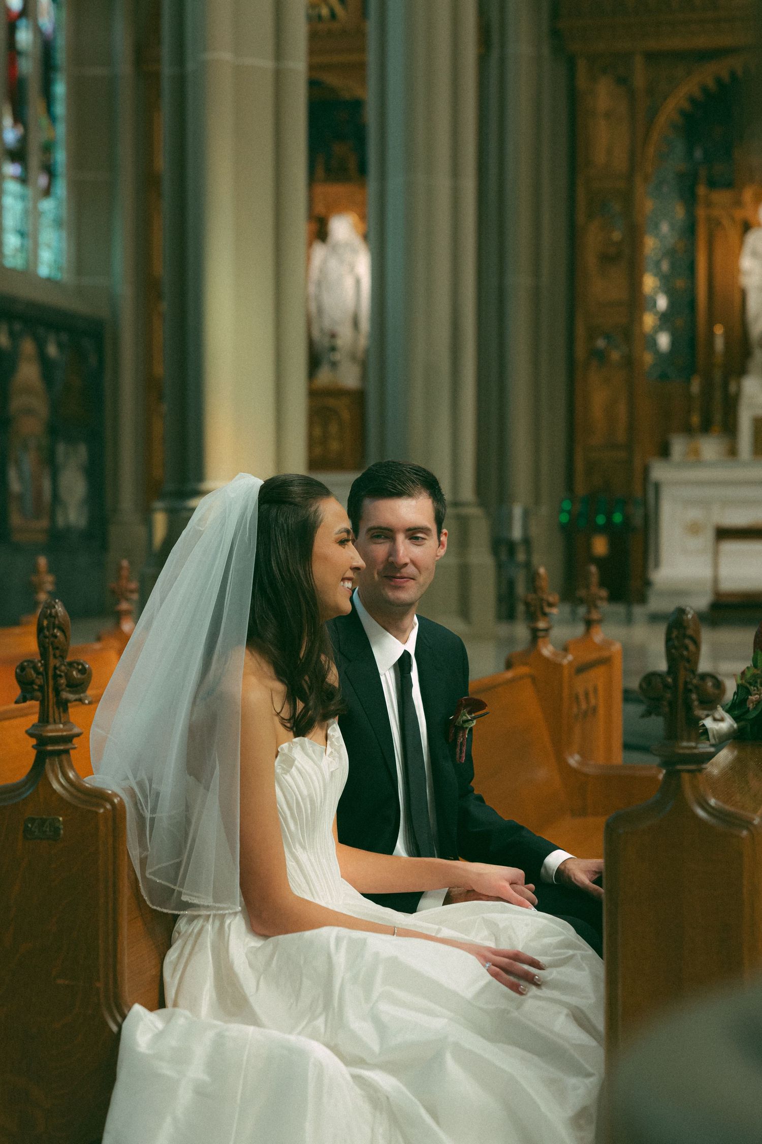 Bride and groom sitting together in church pew during wedding ceremony, bride wearing white gown and veil.