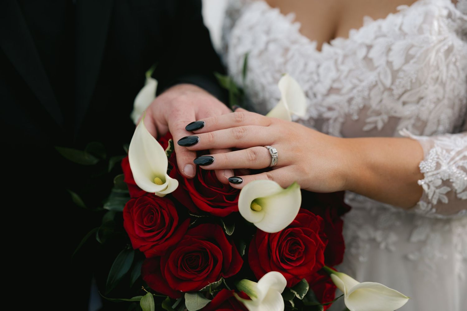 Bride with black nails holds red rose and white calla lily wedding bouquet.