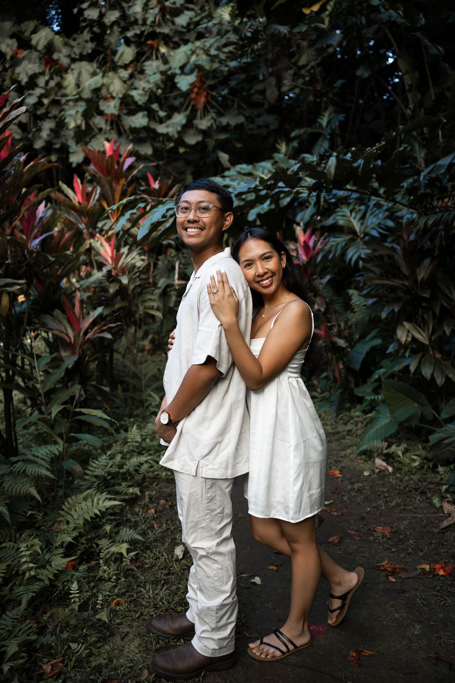 A couple poses together on a garden path surrounded by tropical foliage.