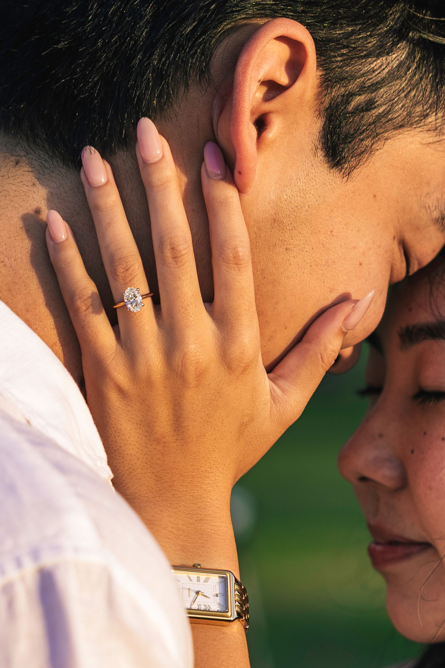 Close up view of two people sharing an intimate moment with an engagement ring visible.