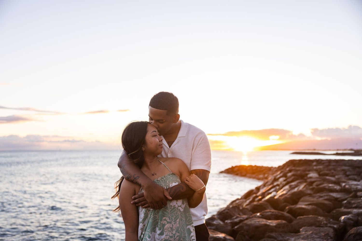 Romantic couple embraces on rocky beach during golden sunset by ocean waves.