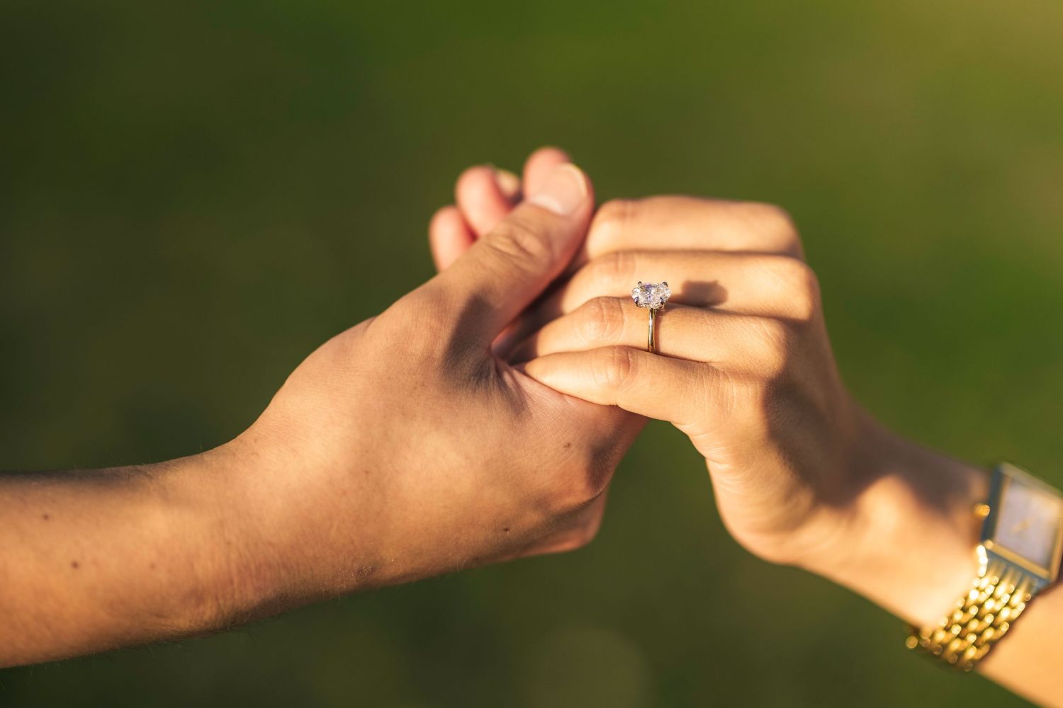 Two hands reaching towards each other with one wearing an engagement ring, photographed in warm sunlight outdoors.