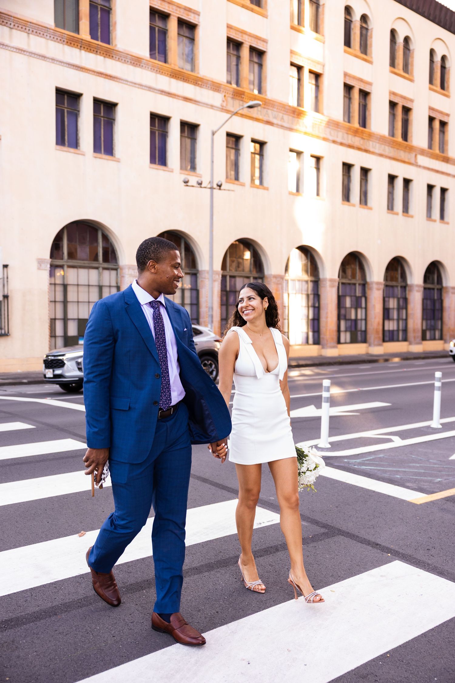 A couple in formal wear crossing a city street crosswalk together.