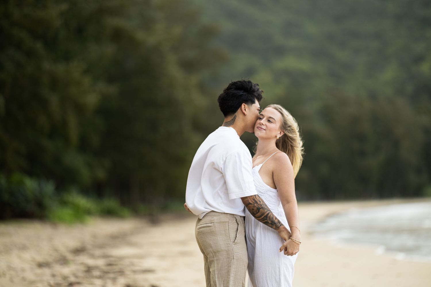 A couple in white outfits sharing a romantic moment on a scenic beach.