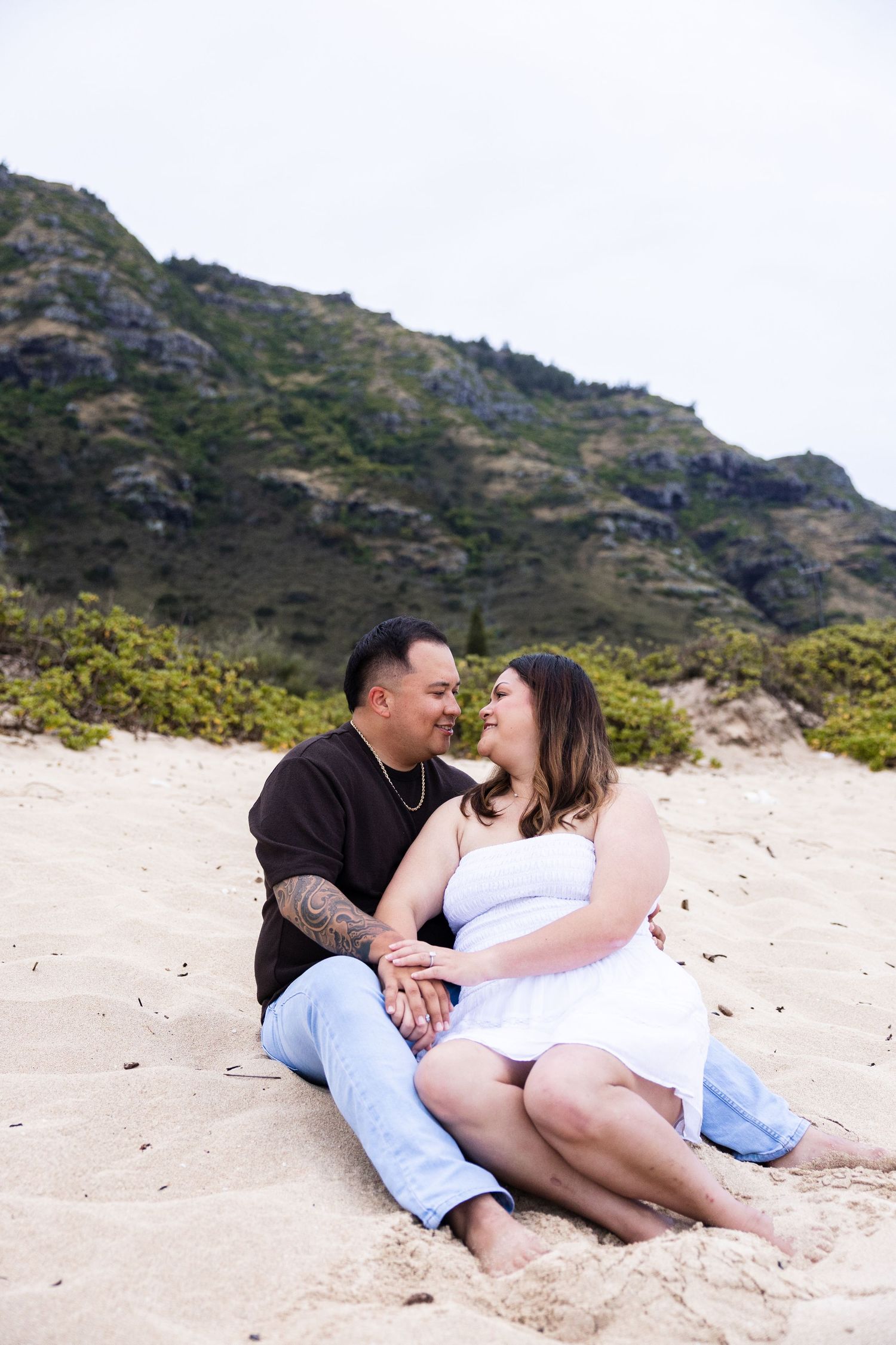 A couple relaxes together on a sandy beach with mountains in the background.