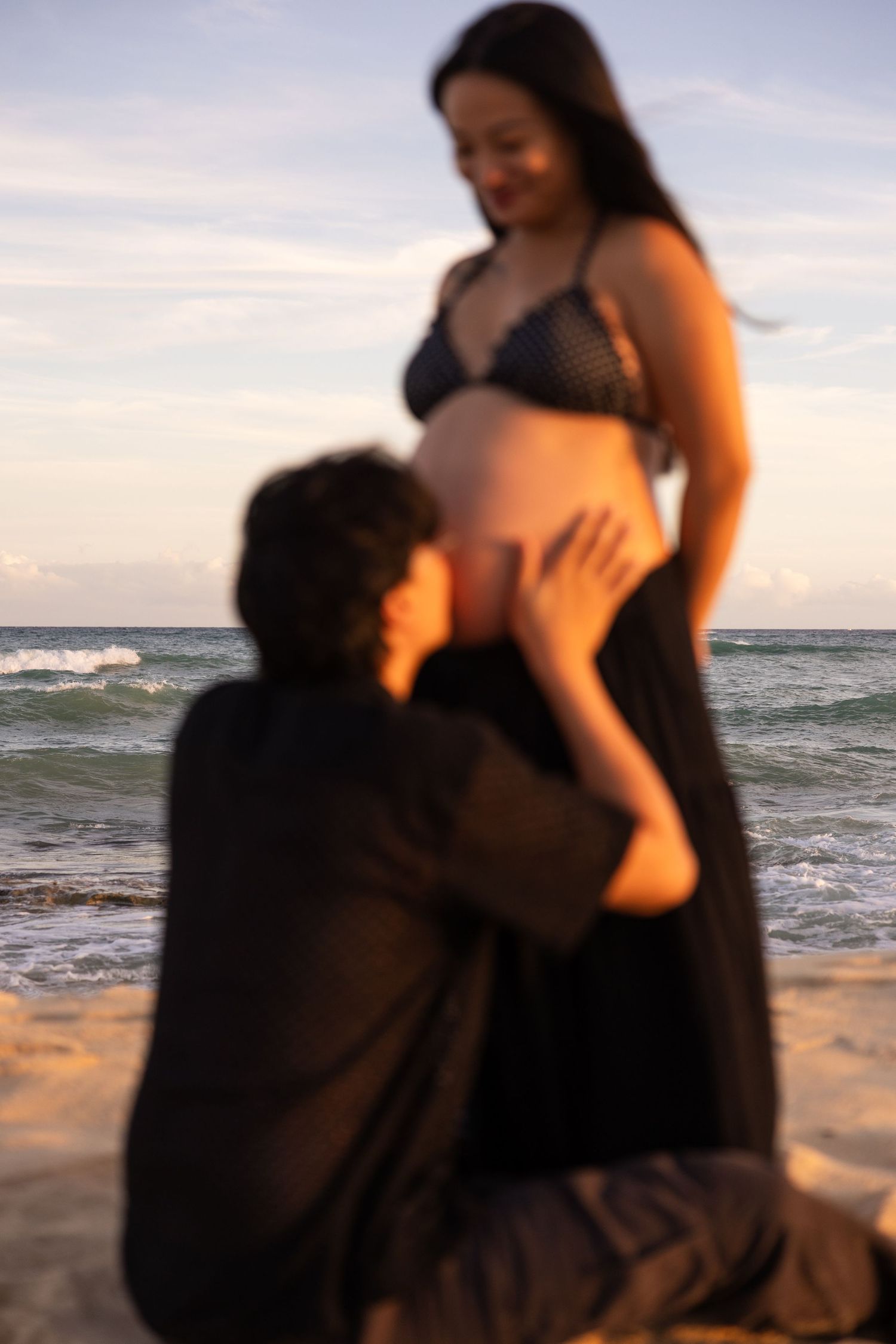 Silhouetted figures embrace on a beach at sunset with ocean waves in the background.