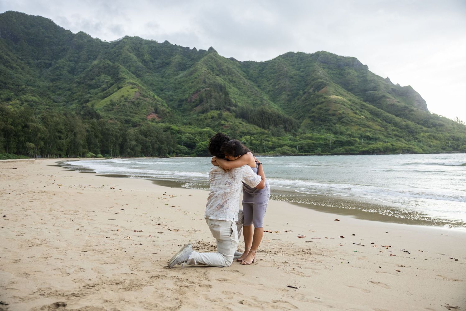 A romantic beach proposal scene with mountains and ocean waves in the background at a scenic Hawaiian beach.