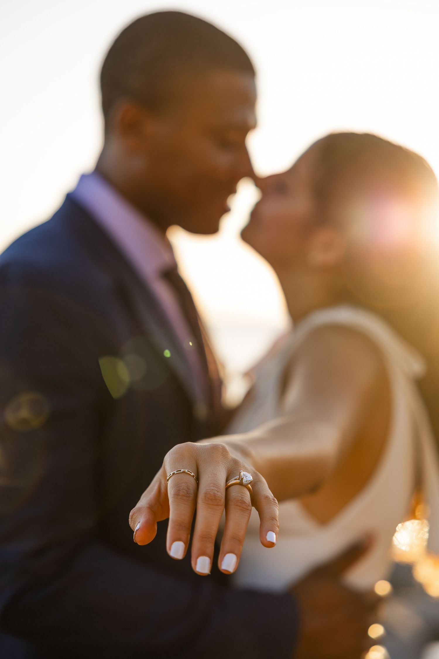 Close-up of intertwined hands showing an engagement ring during a romantic sunset photoshoot.