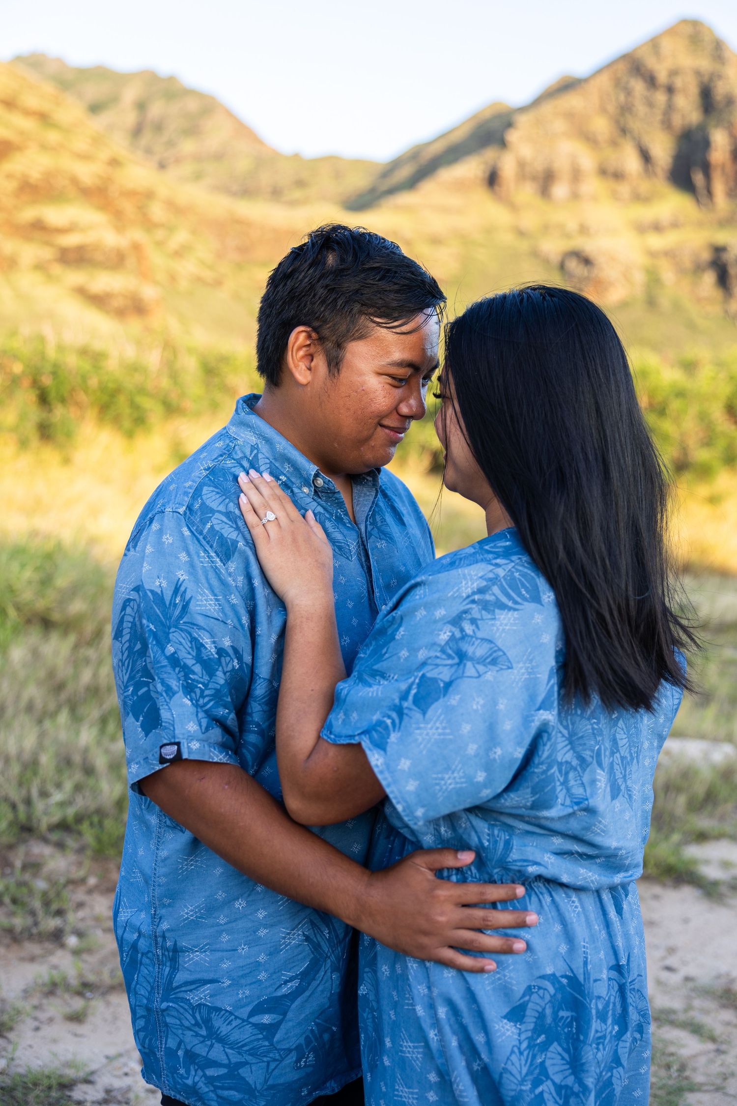 A couple wearing matching blue outfits share intimate moments in a desert landscape at sunset.