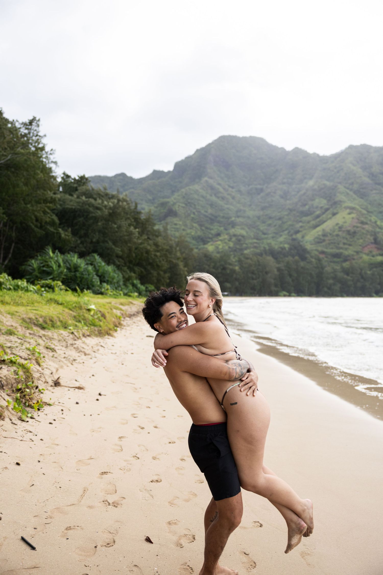 A romantic beach moment captured with dramatic mountain backdrop on a tropical Hawaiian shoreline.