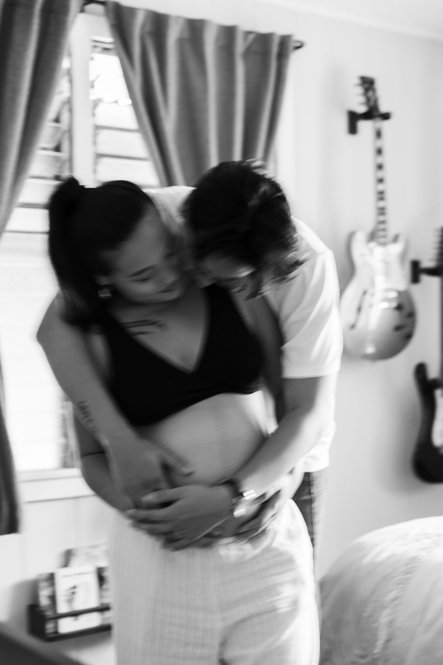 A black and white intimate maternity photo with guitars displayed on wall in background.