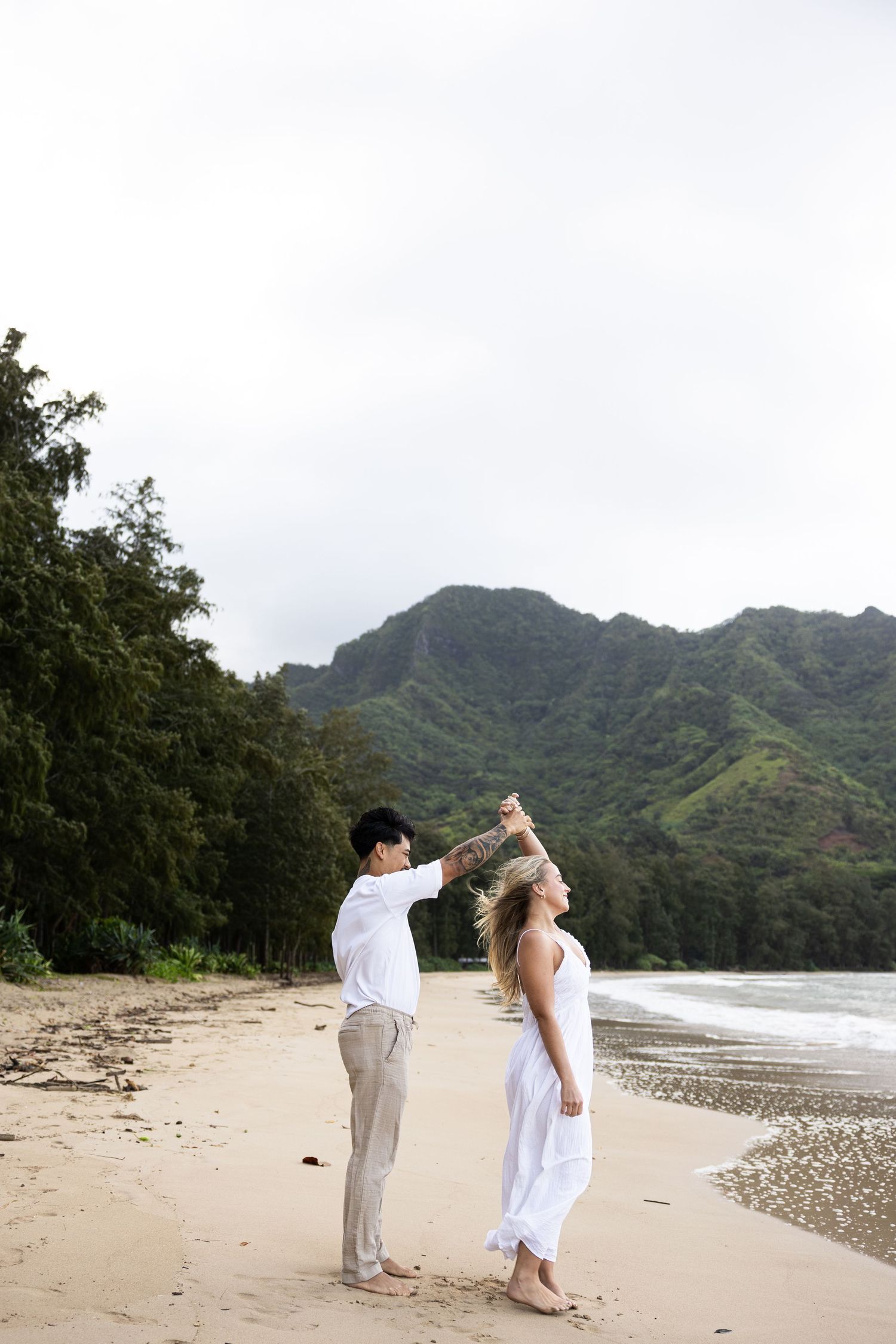 A couple dances playfully on a secluded beach with dramatic mountain scenery in Hawaii.