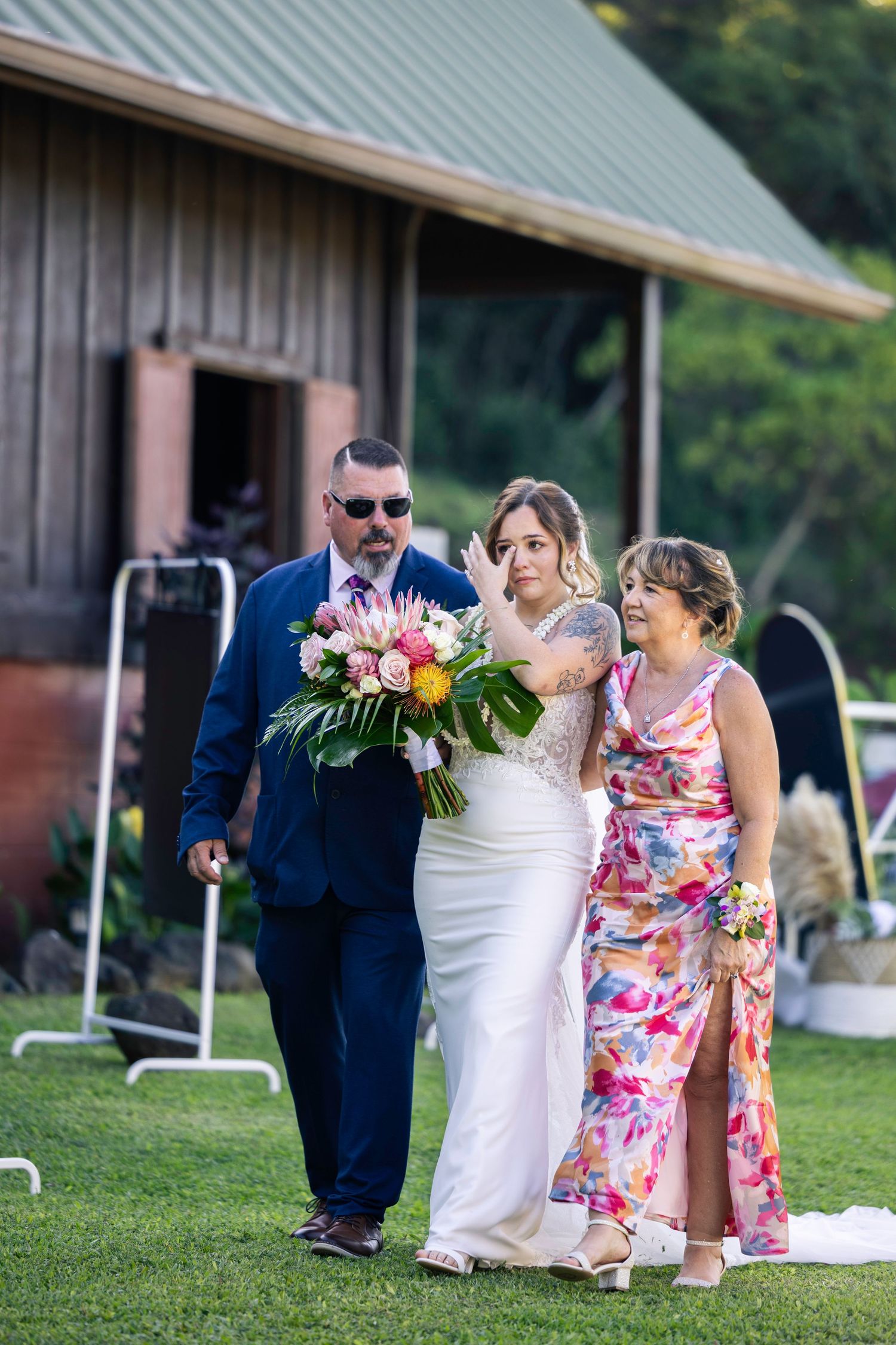 Wedding party members walk and laugh together on grassy grounds near a rustic barn venue.