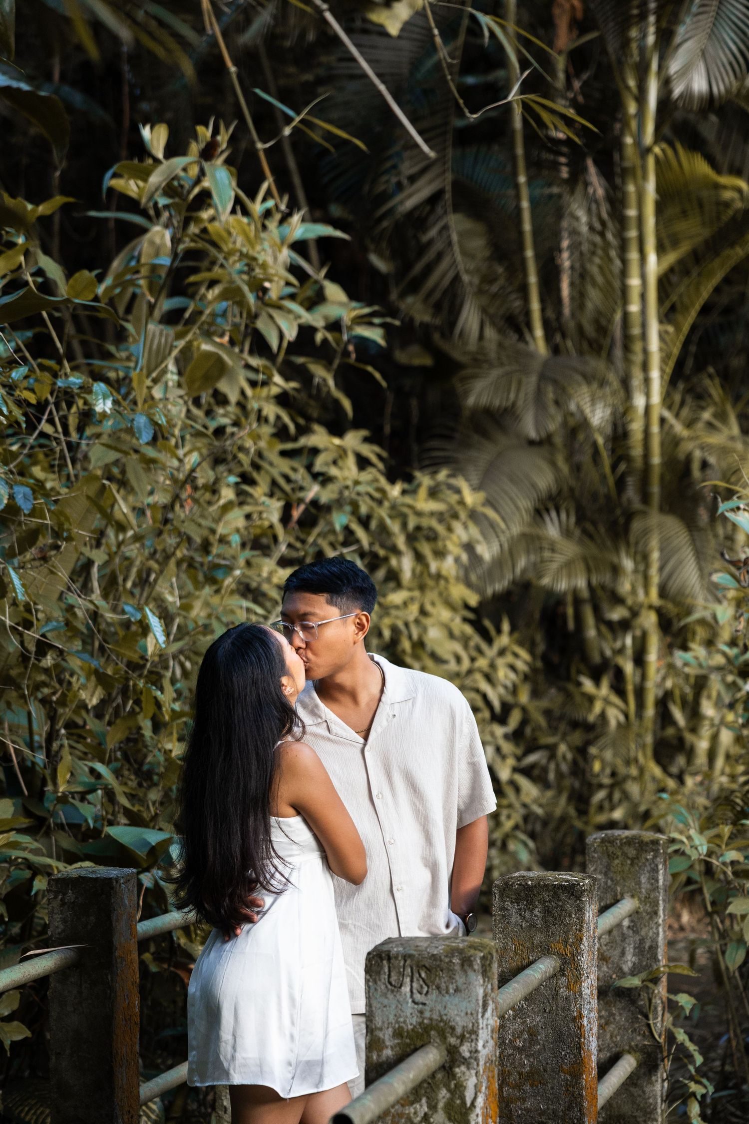 A couple shares an intimate moment on garden steps surrounded by tropical plants.