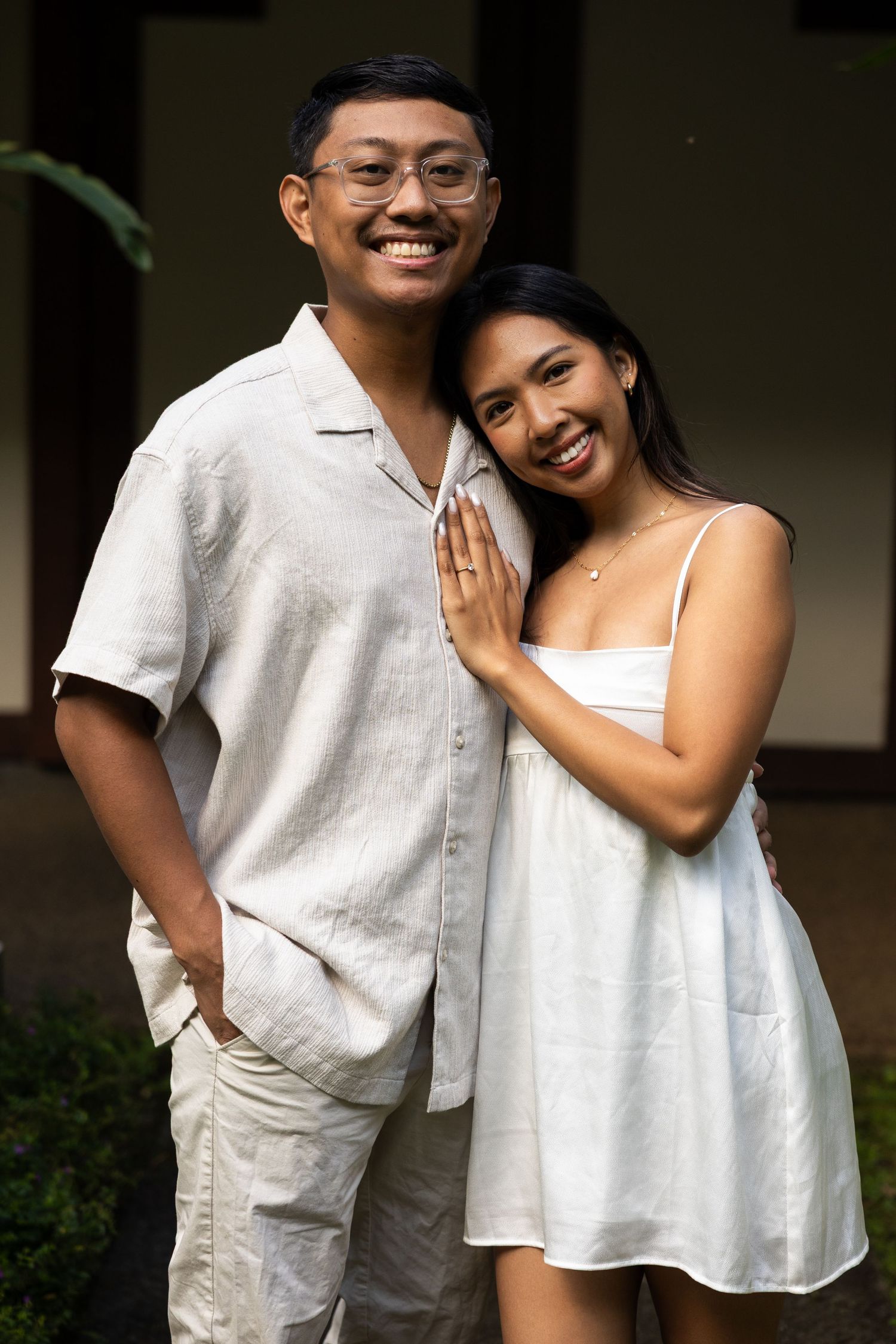 A couple wearing coordinated white outfits embrace and smile while posing together outdoors.