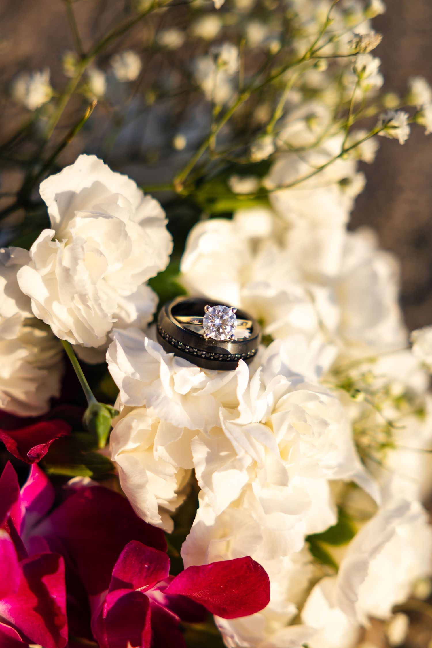 A sparkling diamond engagement ring nestled among delicate white and deep red rose petals in soft lighting.