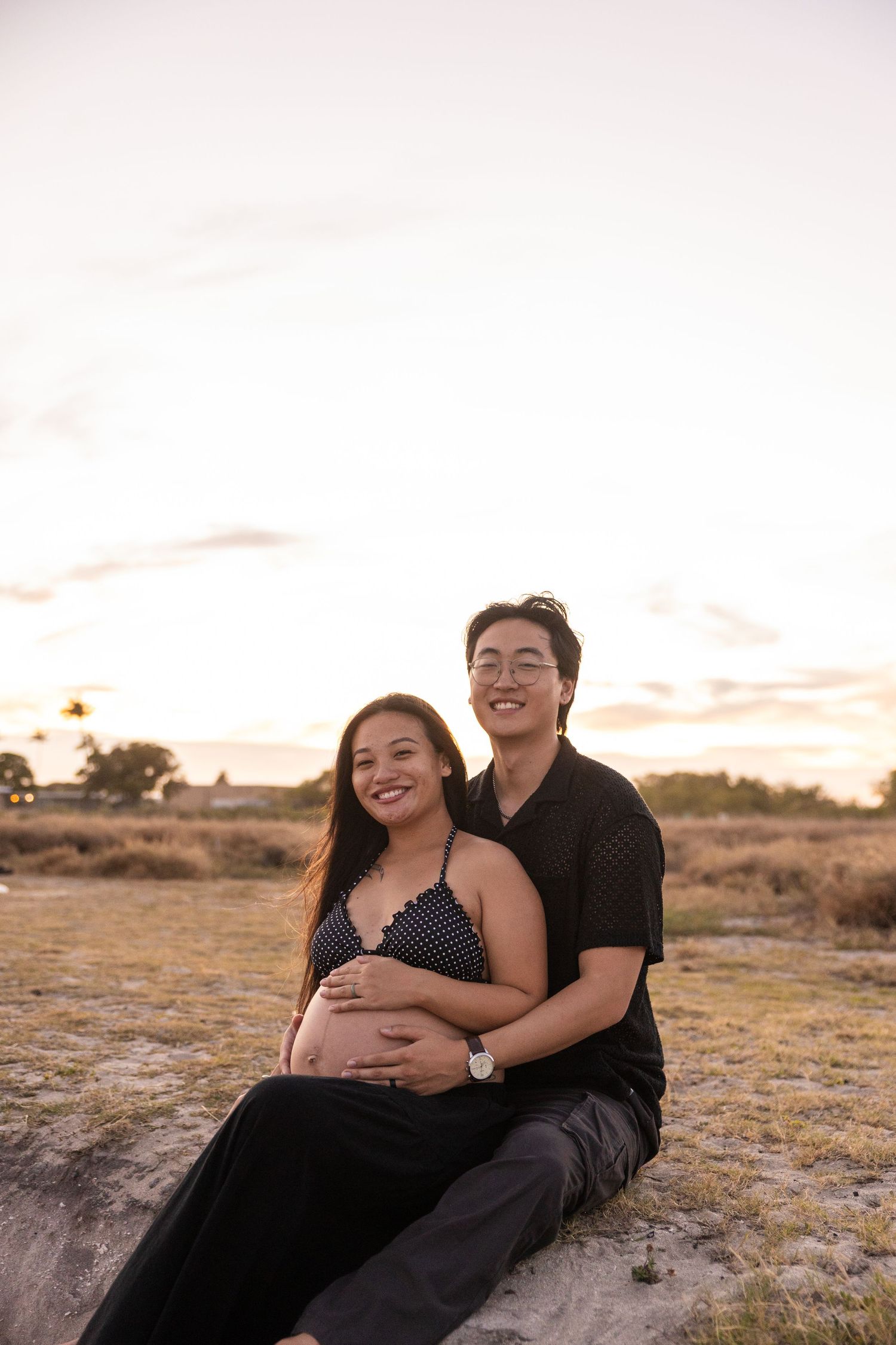 A couple shares tender moments at sunset in an outdoor desert setting with rocks and dry terrain.