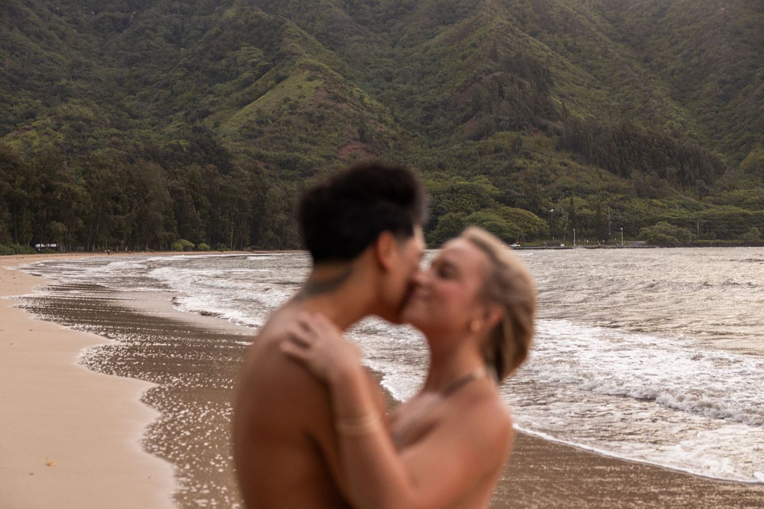 Intimate beach moment with dramatic Hawaiian mountains in background.