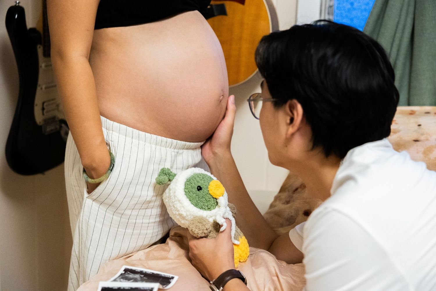 A close-up shot in a bedroom showing someone placing a drink near a pregnant belly in white striped pants.