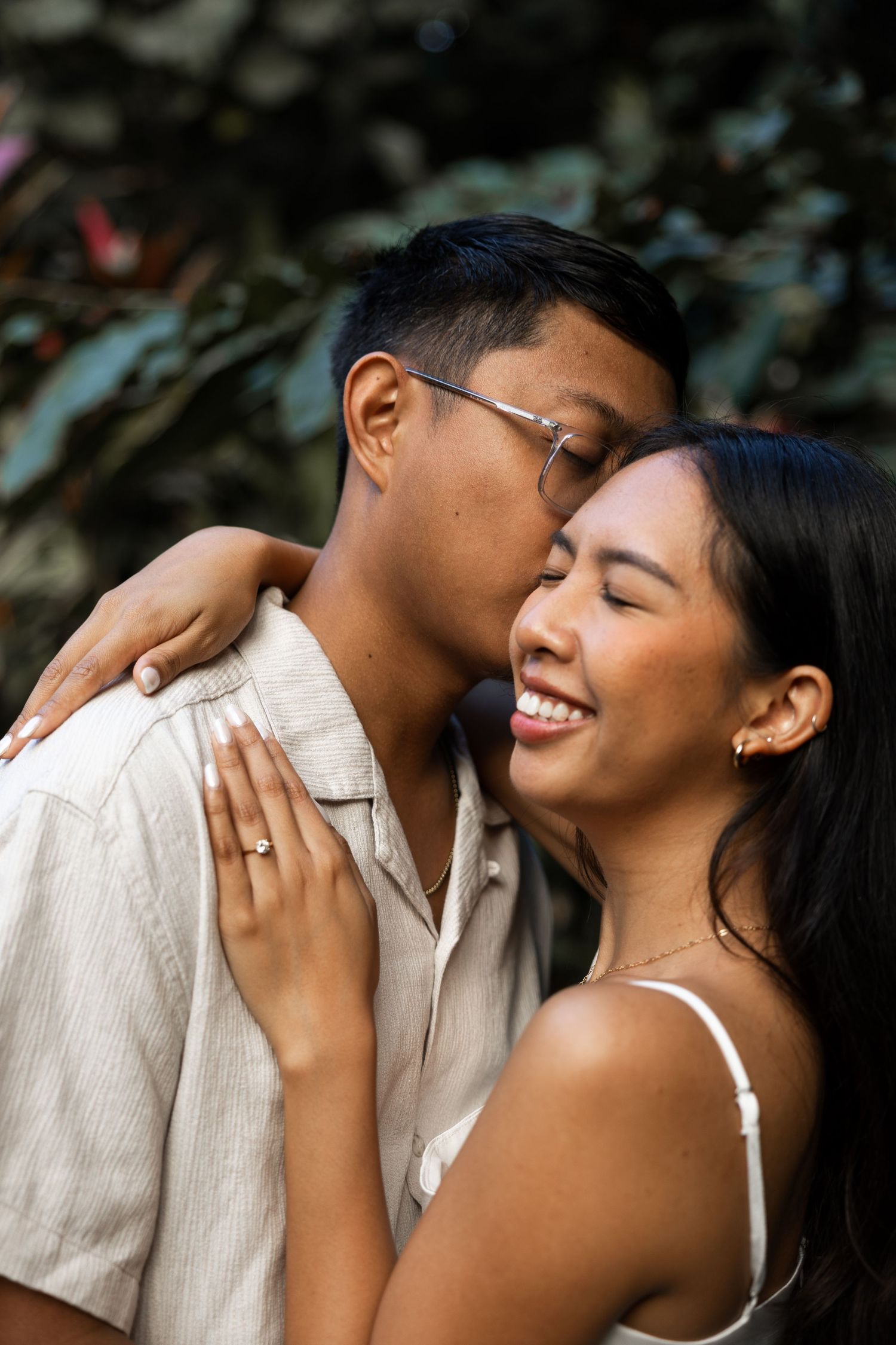 A couple shares an intimate moment while dressed in white against a garden backdrop.