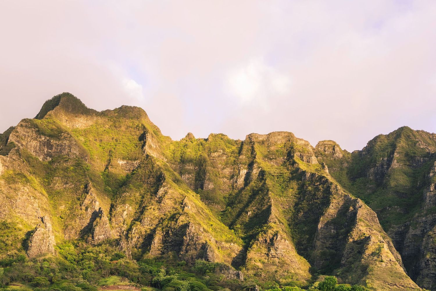 Panoramic view of rugged mountain peaks glowing golden in sunset light along the Na Pali Coast of Kauai, Hawaii.