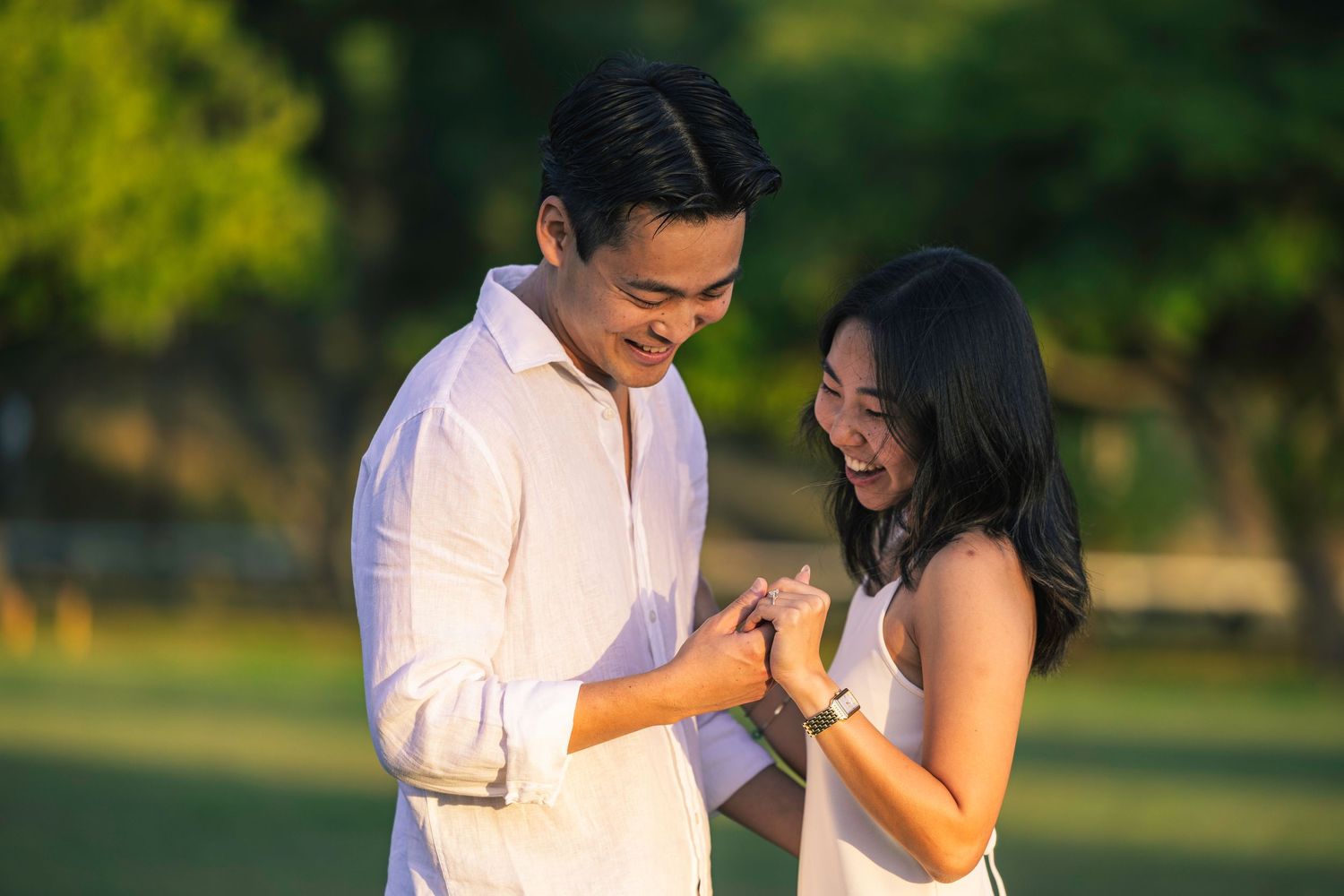Romantic couple in white clothing embracing during golden hour in a park setting.