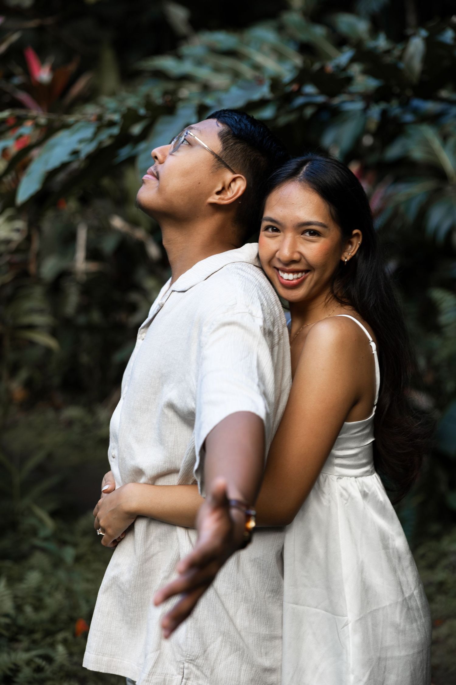 A couple shares a playful back-to-back pose in a tropical garden setting.
