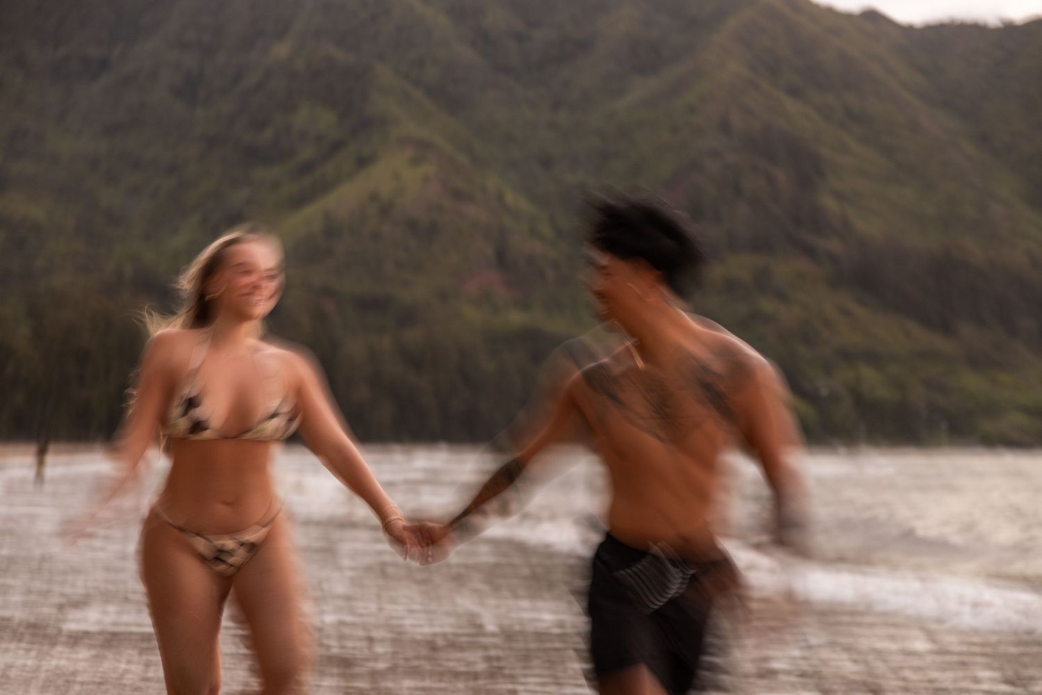 A blurred motion shot captures a couple running joyfully on a Hawaiian beach.