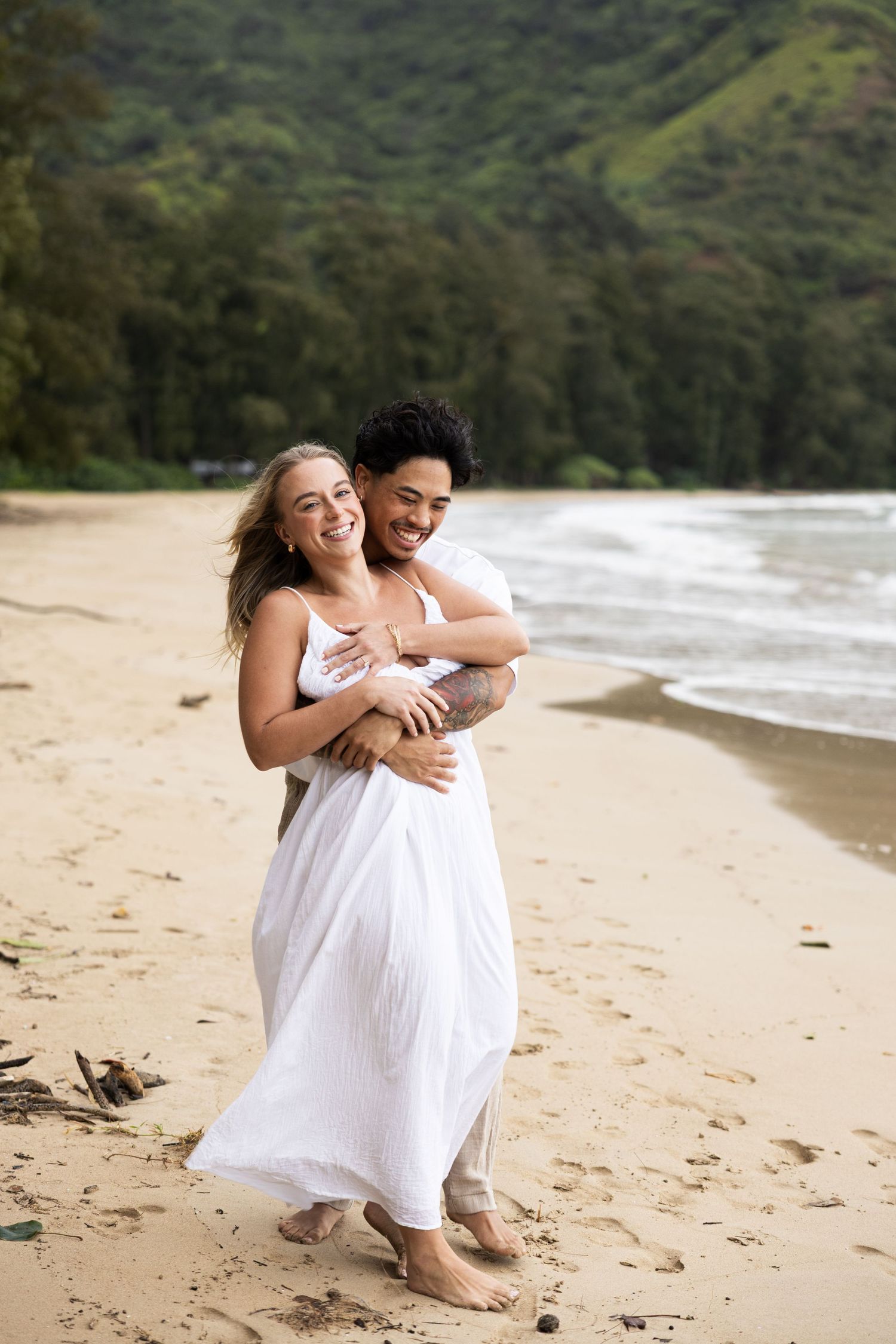 A couple shares a joyful moment together on a tropical beach with mountains in background.