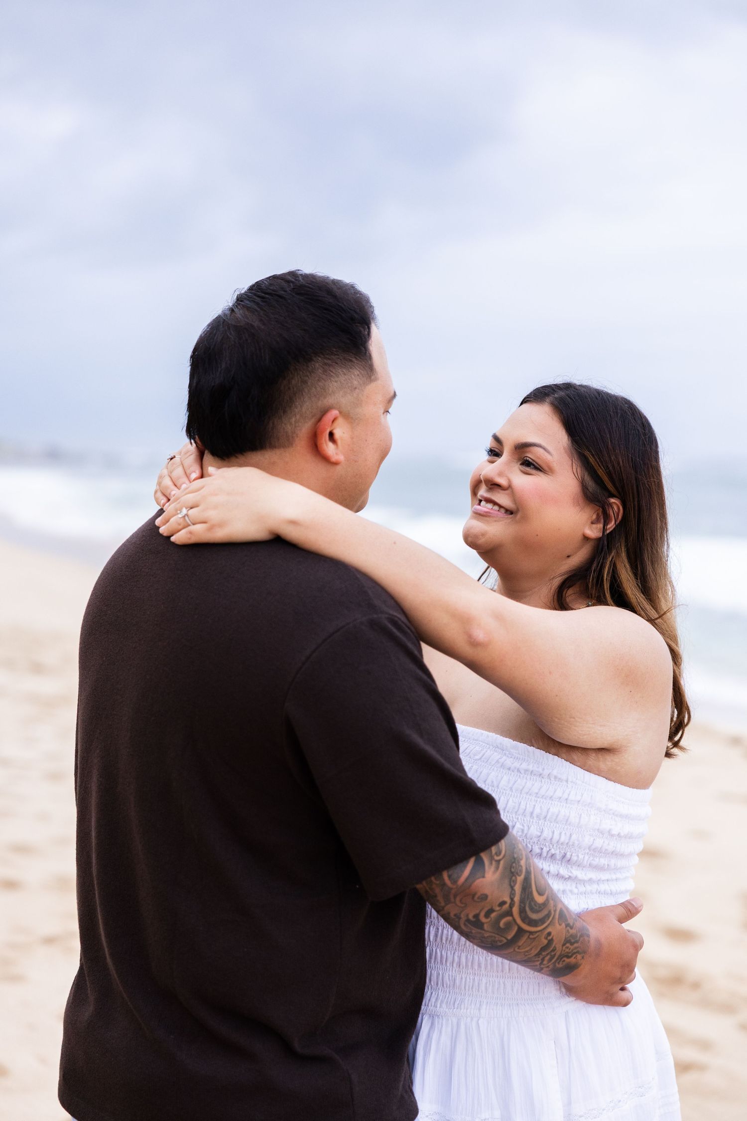 A couple embraces lovingly on a sandy beach during an engagement photo session.