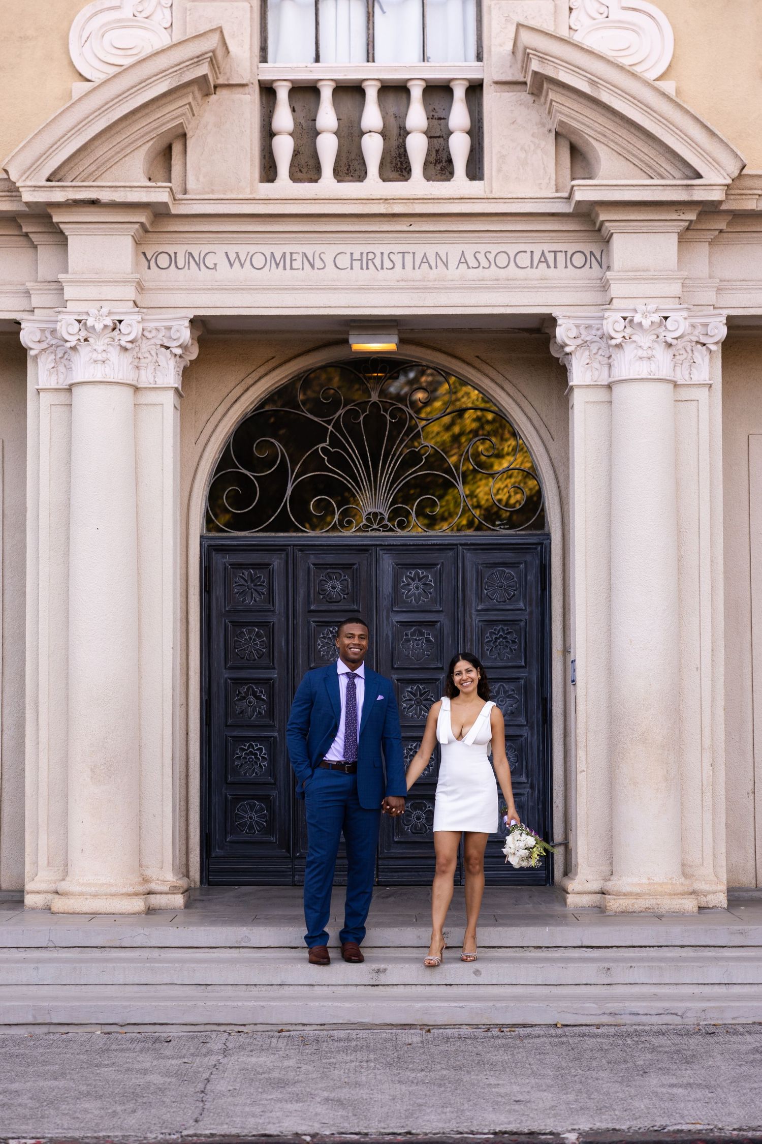 A bride and groom pose at the entrance of the Young Women's Christian Association building.