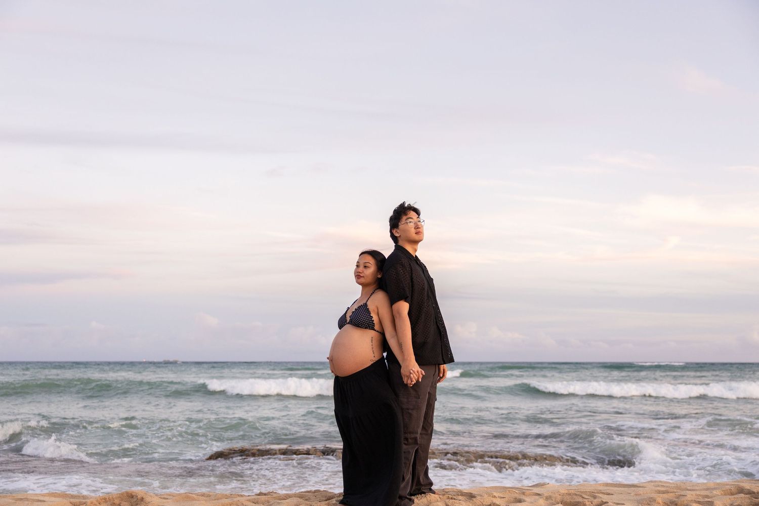 A couple embraces while watching the sunset on a scenic beach with waves crashing in the background.