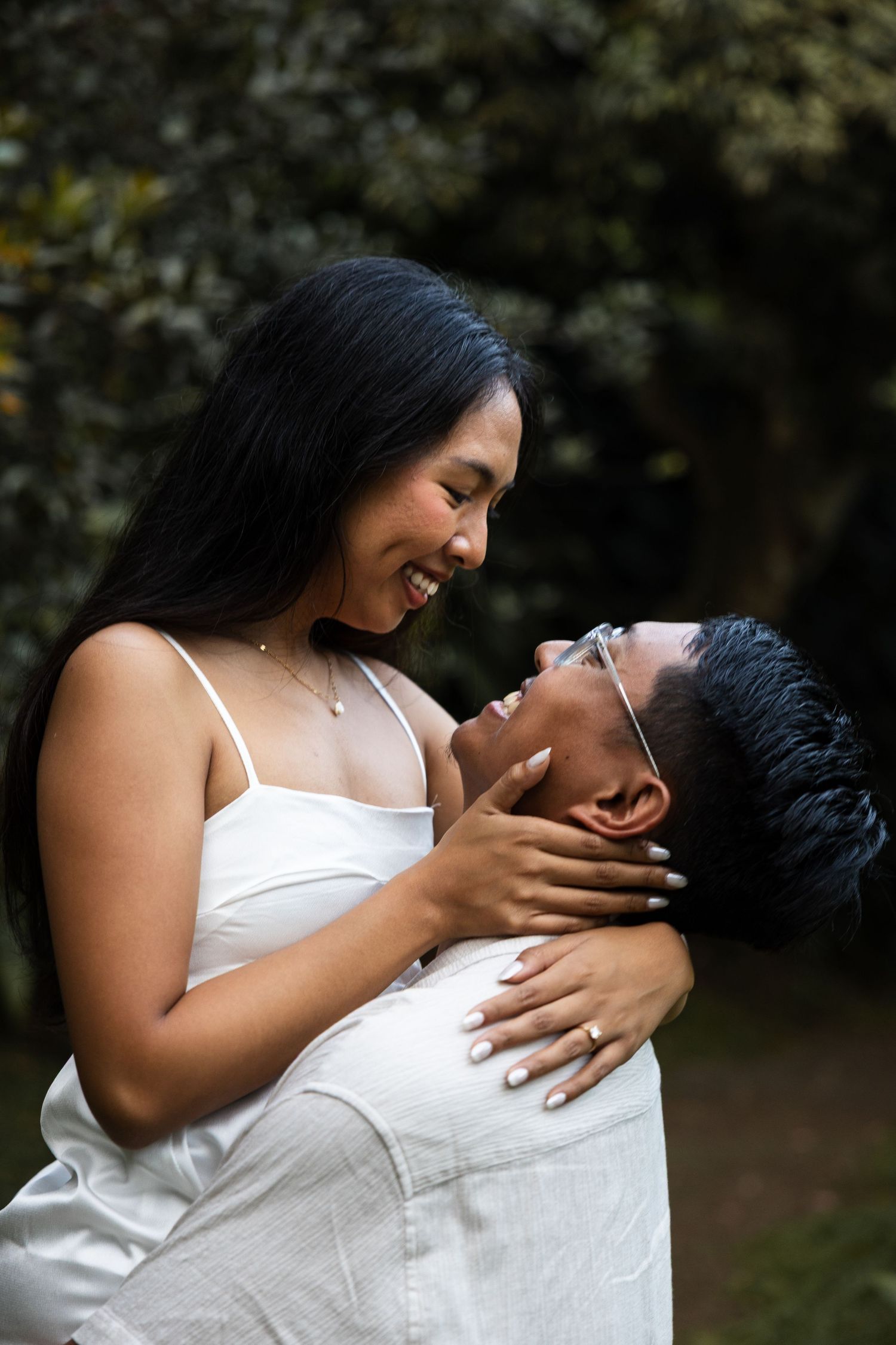 A happy couple shares a playful embrace while wearing white outfits in a garden.