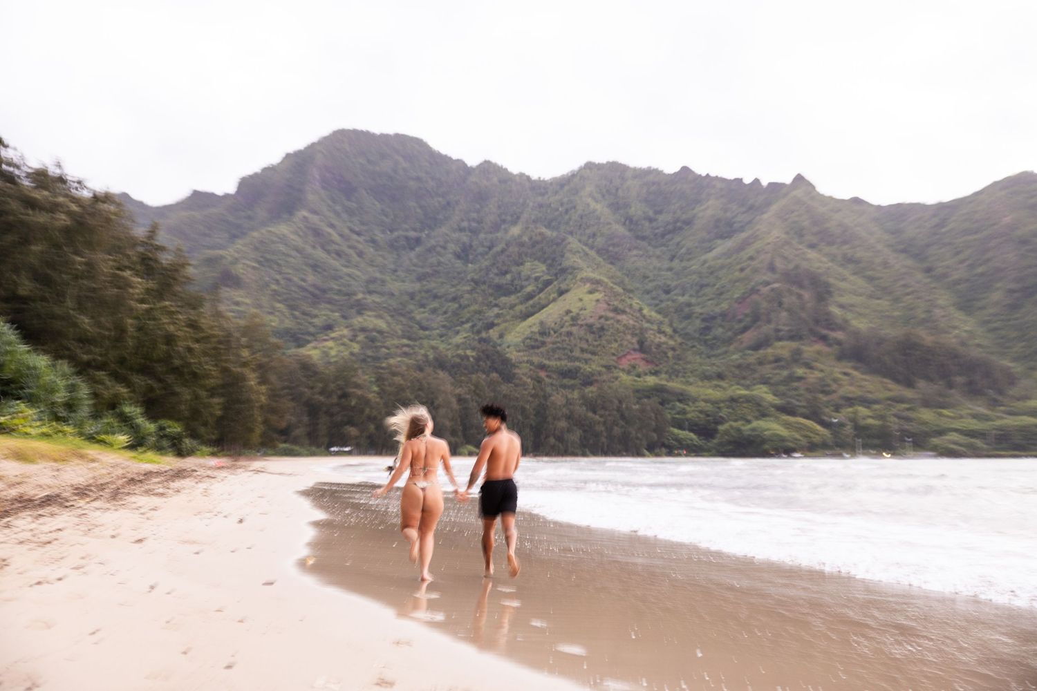 Two beachgoers walking along shoreline with majestic mountain landscape in Hawaii.