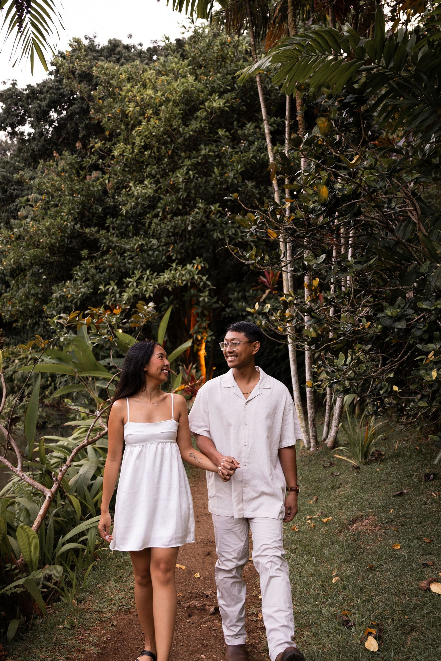 A couple takes a romantic stroll along a tropical garden path surrounded by palm trees.