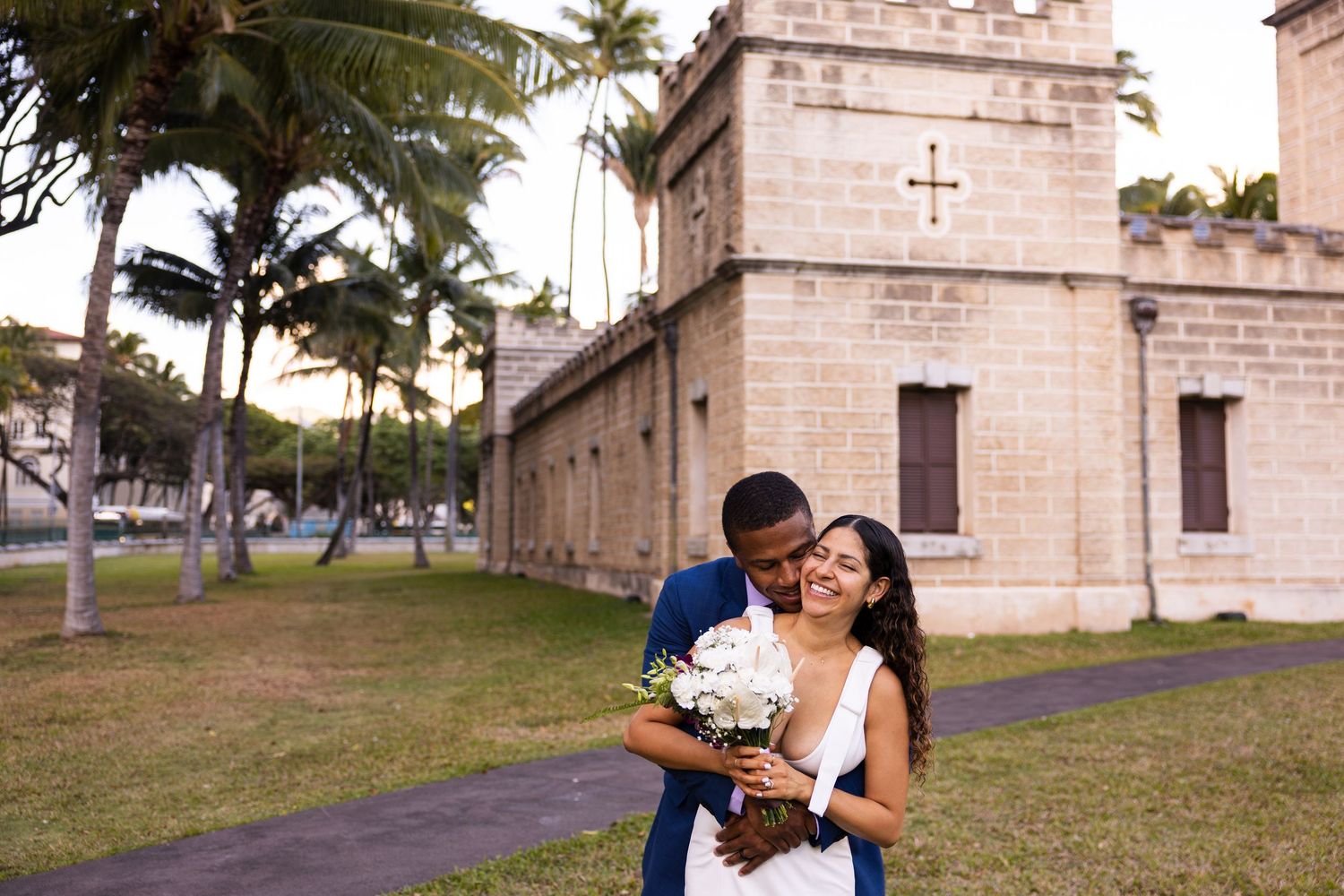 A couple shares a romantic moment outside a historic building with palm trees.