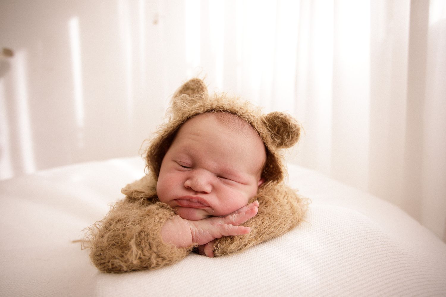 Sleeping newborn wearing a teddy bear hat against white background.