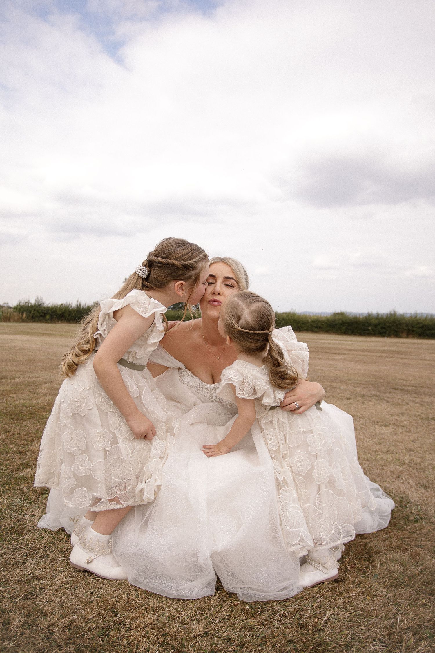 Sweet moments shared in white dresses against a cloudy sky.