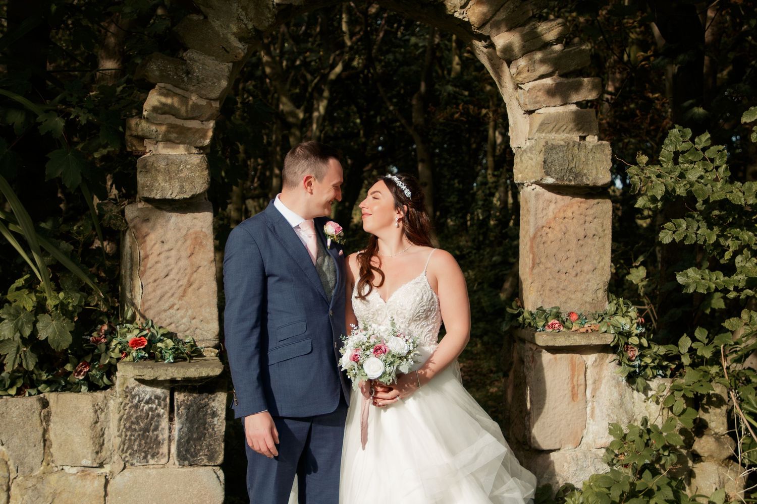 Romantic wedding moment under stone archway in garden setting.