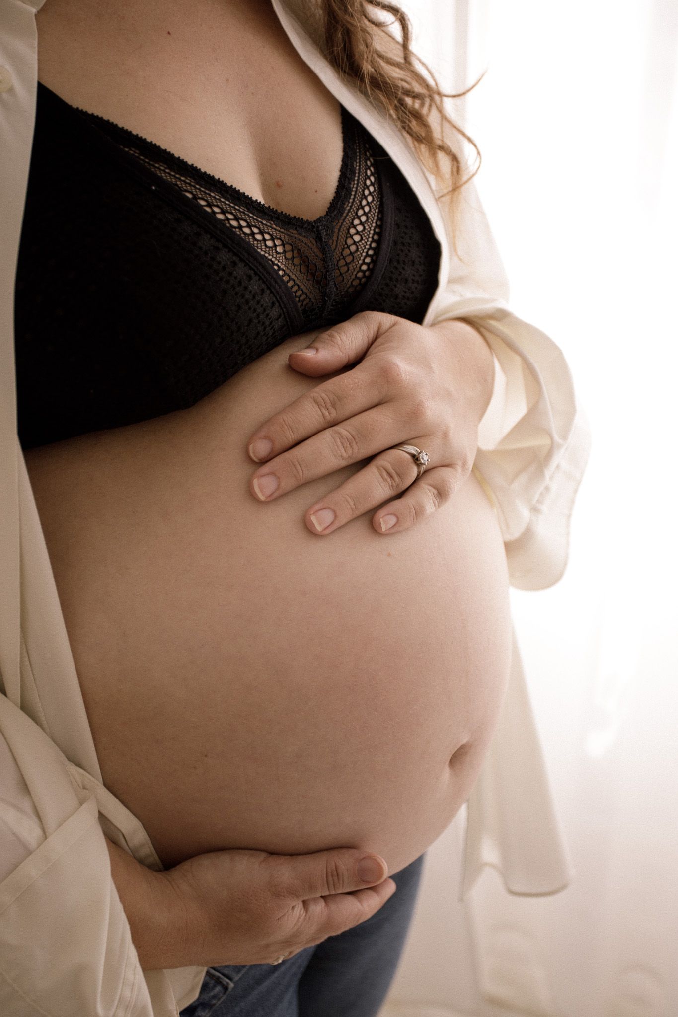 Artistic maternity photo of pregnant belly with hands cradling bump in black lingerie.