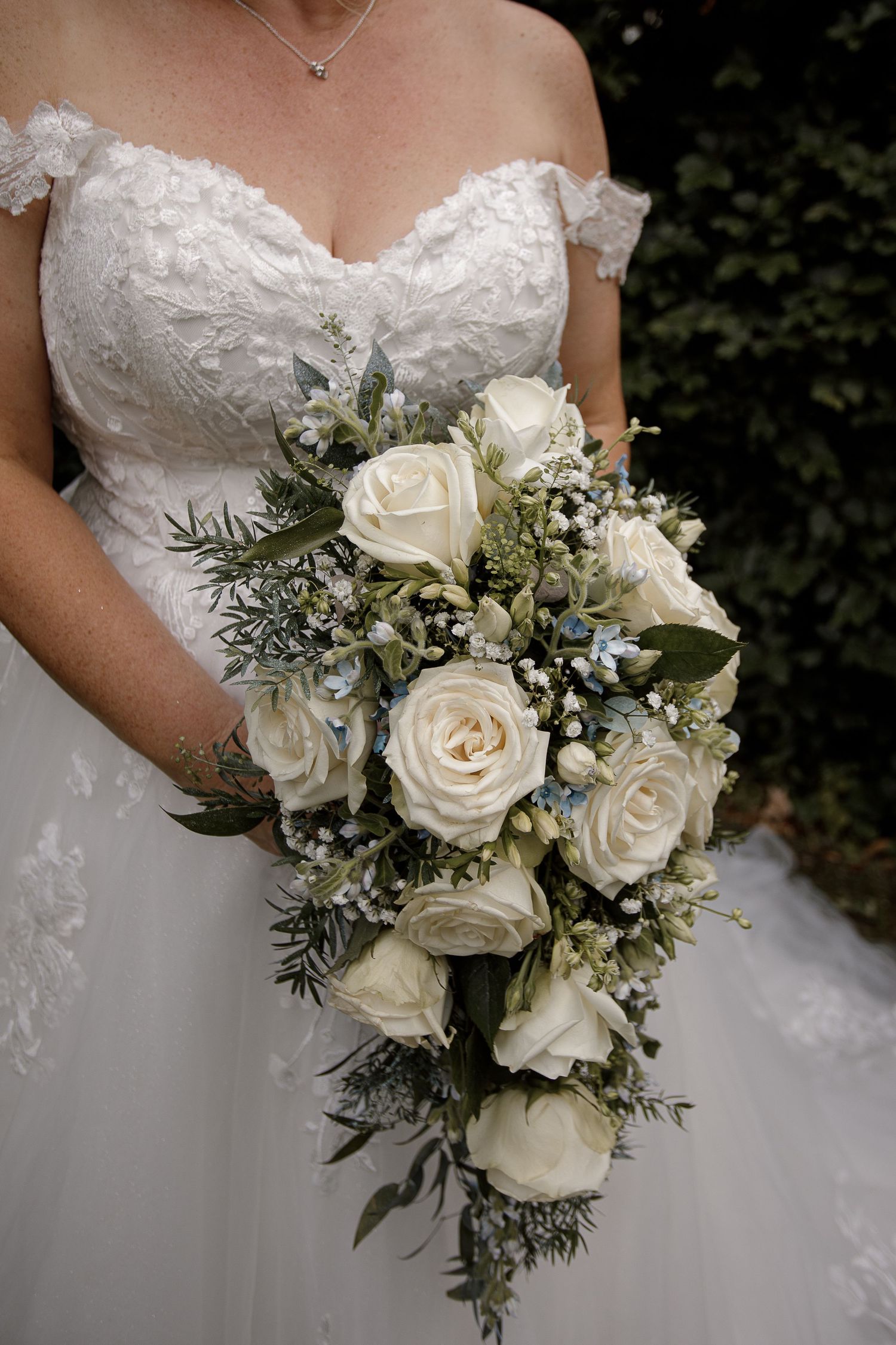 Close-up of an elegant white rose and greenery wedding bouquet with delicate blue accents.
