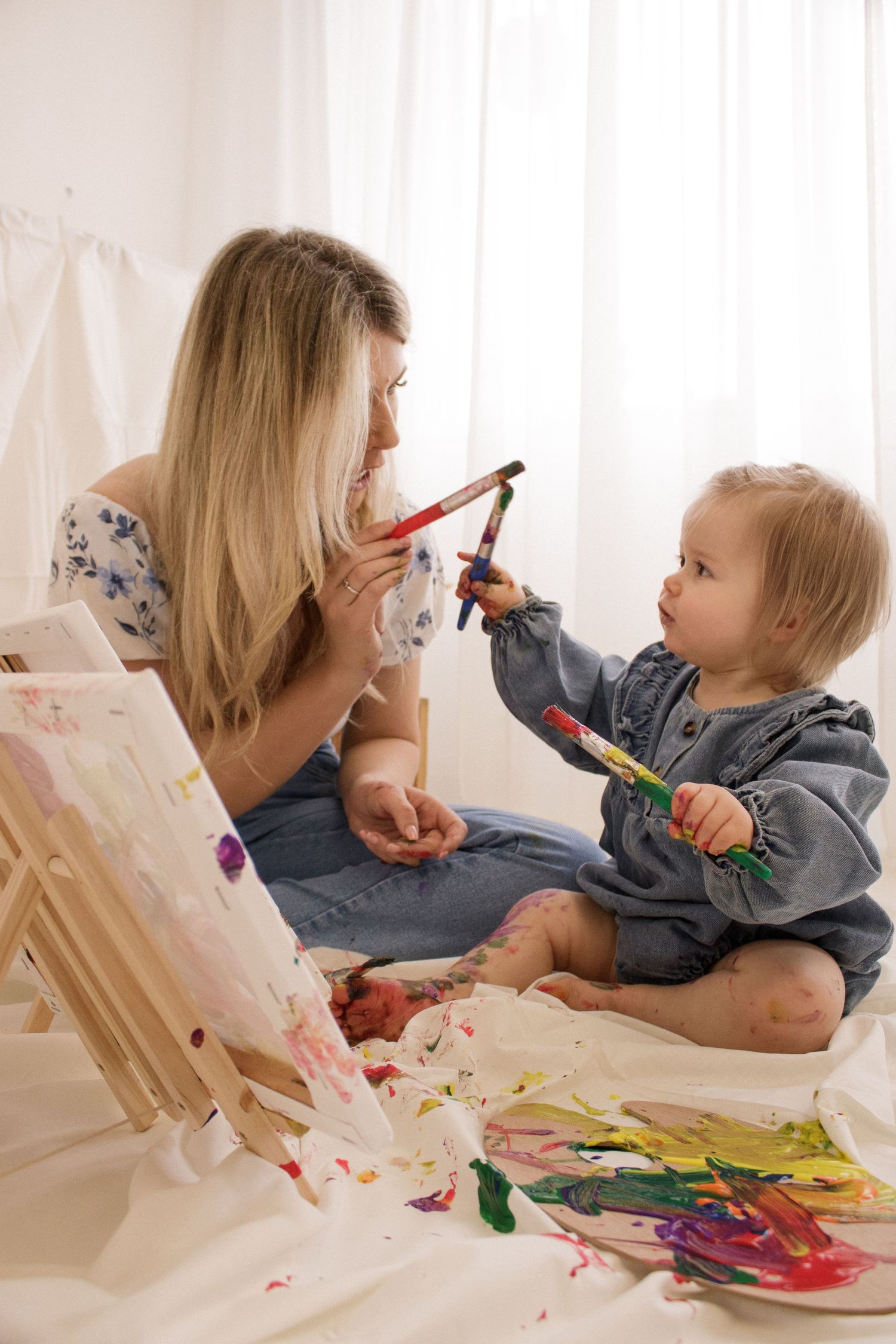 Parent and child painting together on easel with colorful paints.